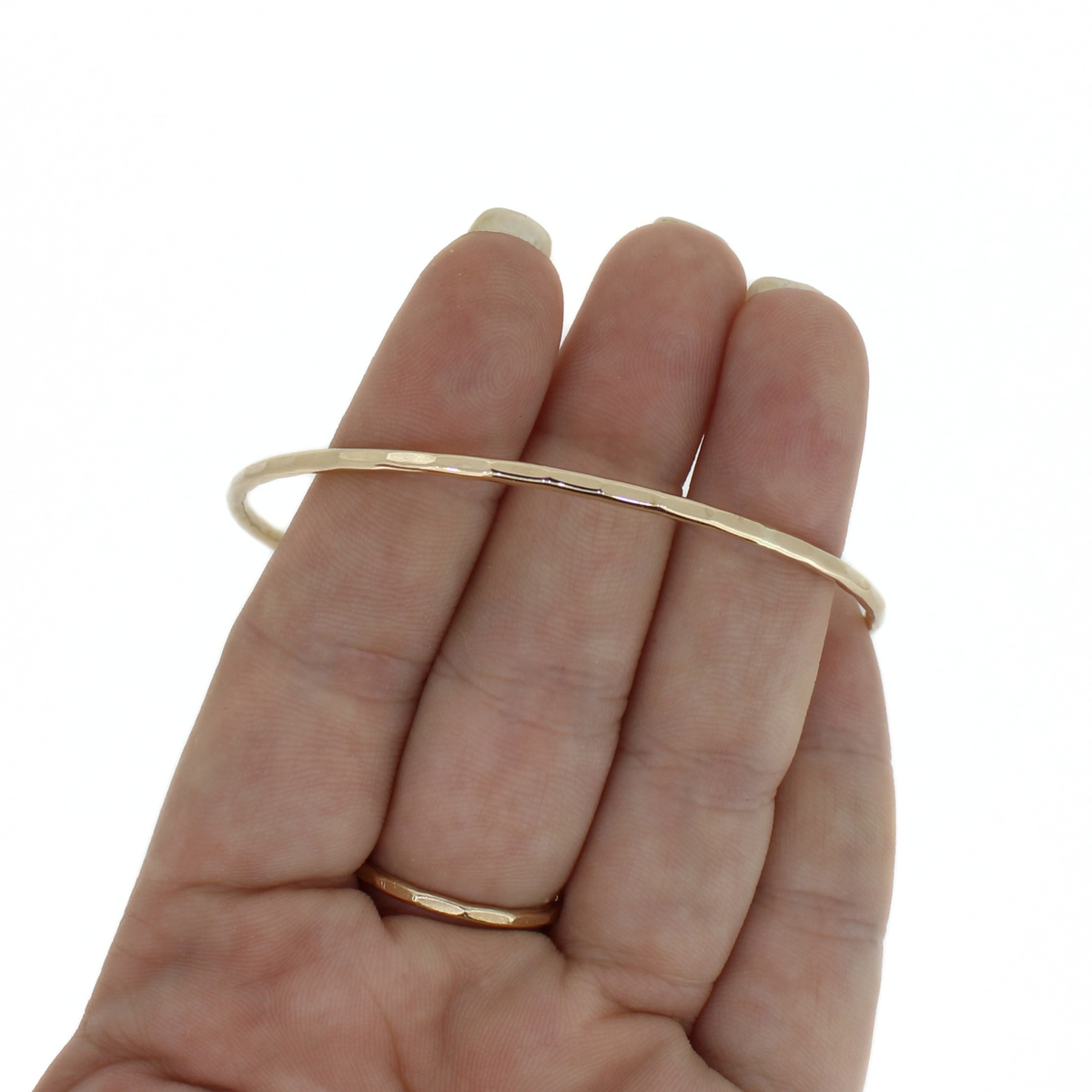 A thin, polished gold bangle bracelet held across a person's hand against a plain white background.