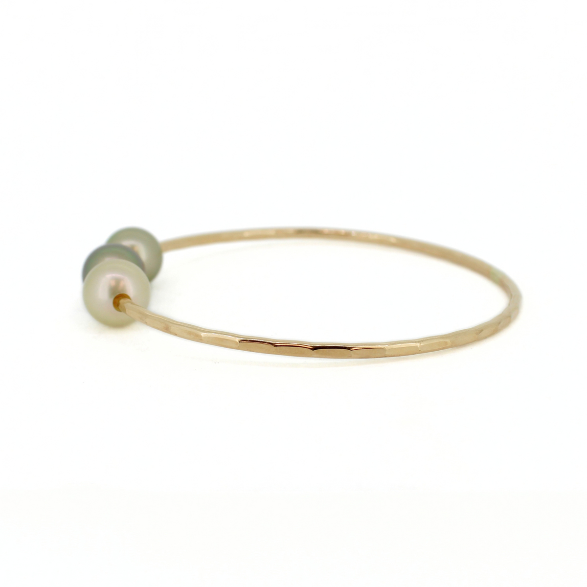 A delicate hammered gold bangle bracelet featuring three small, round, iridescent pearls, set against a plain white background.