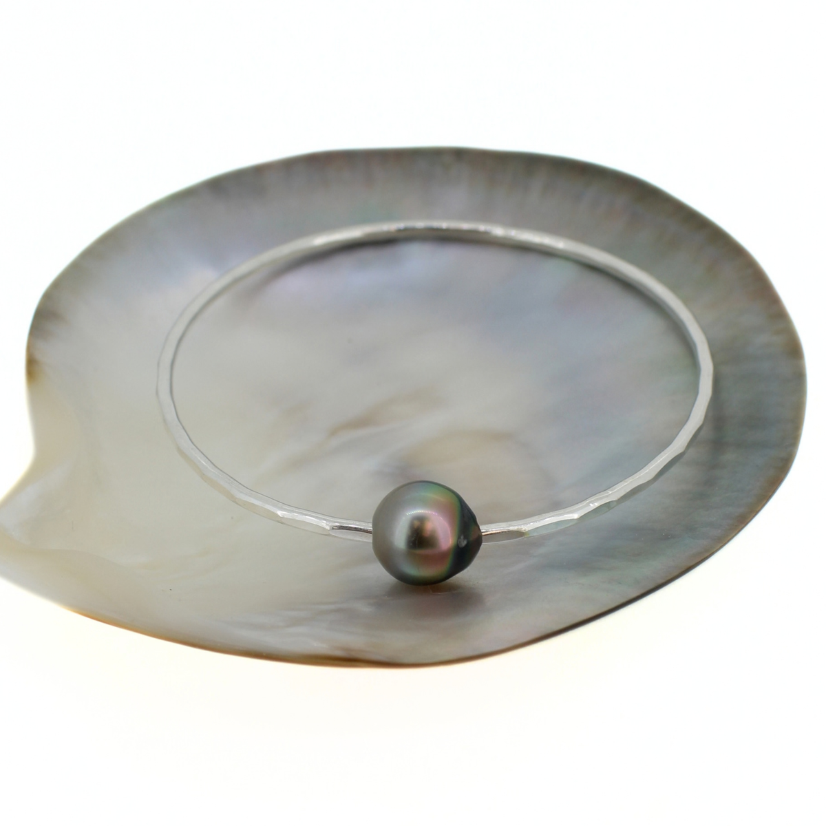 Sterling silver bangle bracelet with a gray Tahitian pearl displayed on a mother of pearl shell