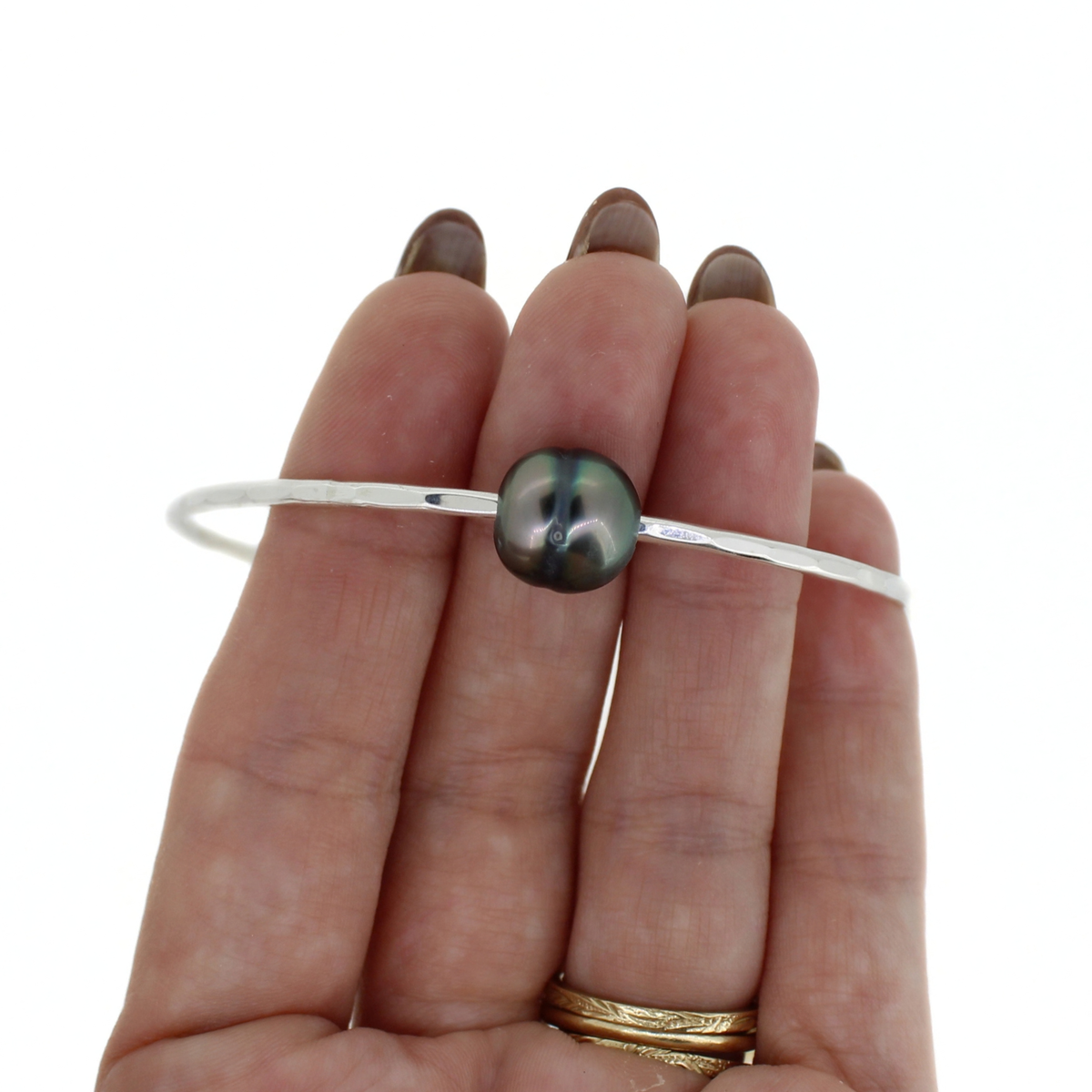 Sterling silver hammered bangle bracelet with Tahitian pearl shown on a persons fingers for size reference 