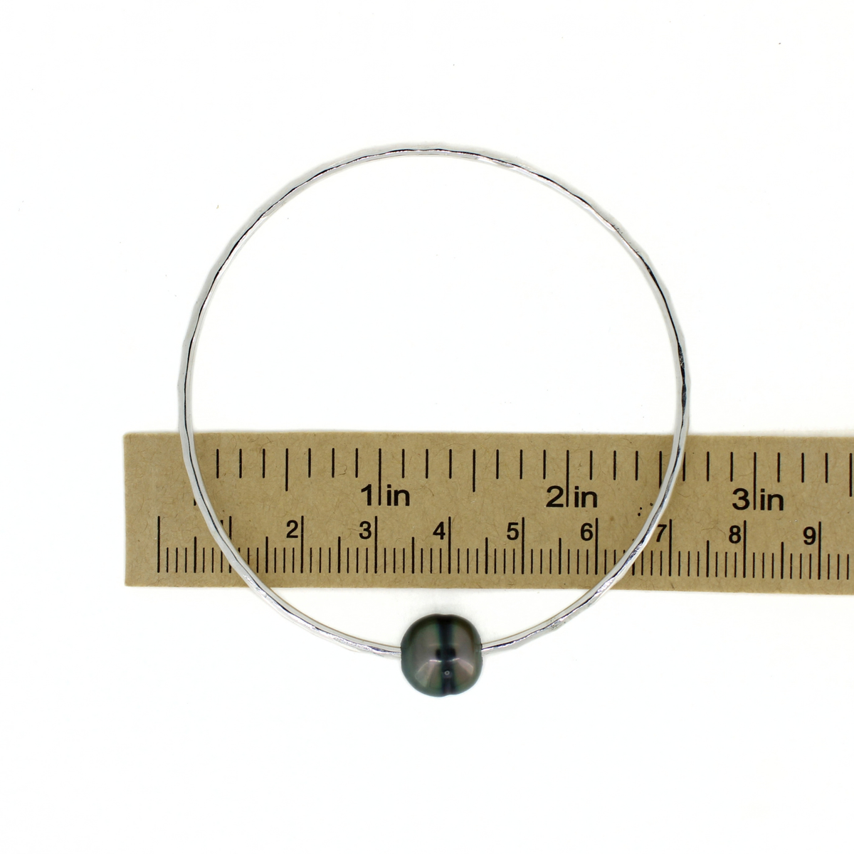 Silver round bangle bracelet with a dark Tahitian pearl shown over a ruler for size reference