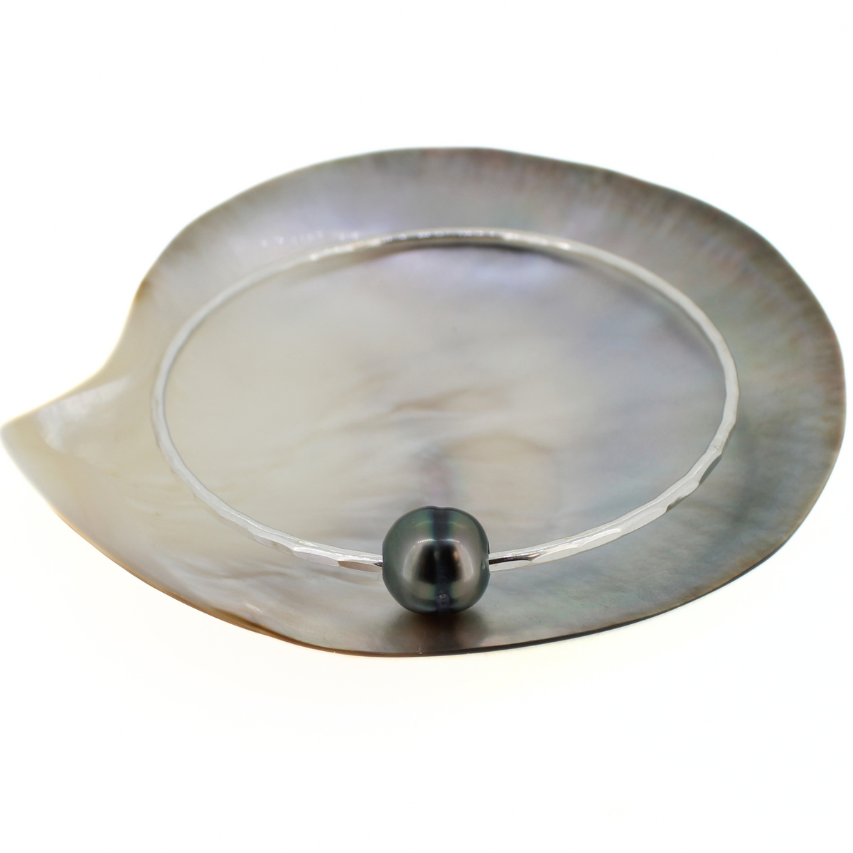 Sterling silver bangle bracelet with a dark Tahitian pearl displayed on a mother of pearl shell