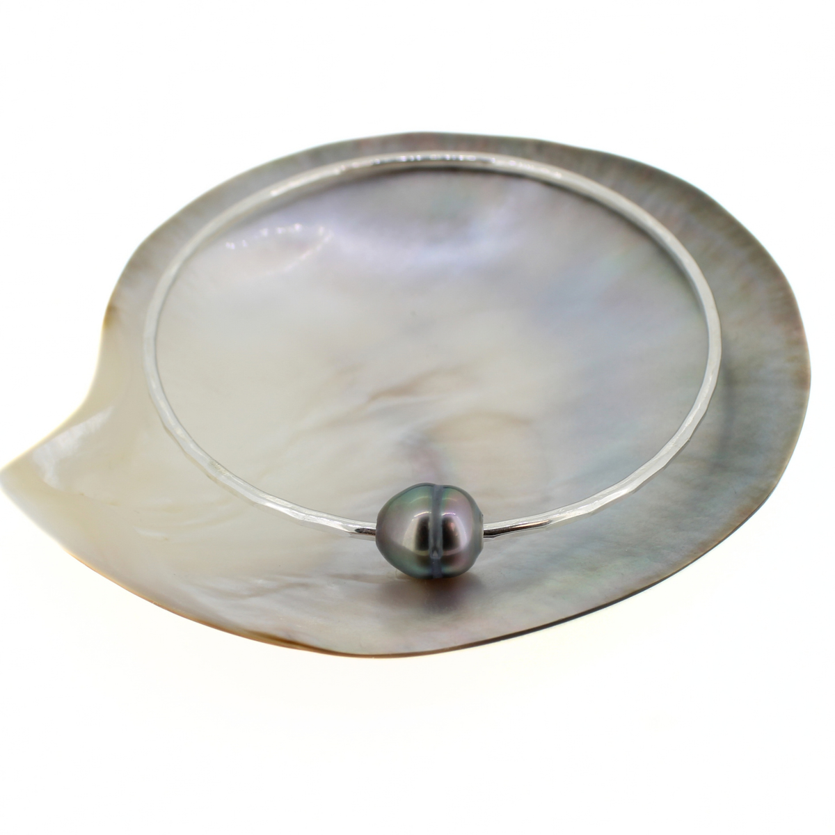 Sterling silver round bangle bracelet with a Tahitian pearl displayed on a mother of pearl shell