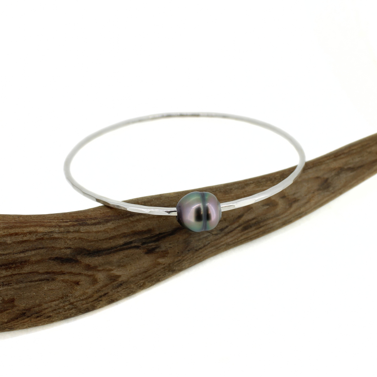 Silver bangle bracelet with a Tahitian pearl displayed on a piece of driftwood 