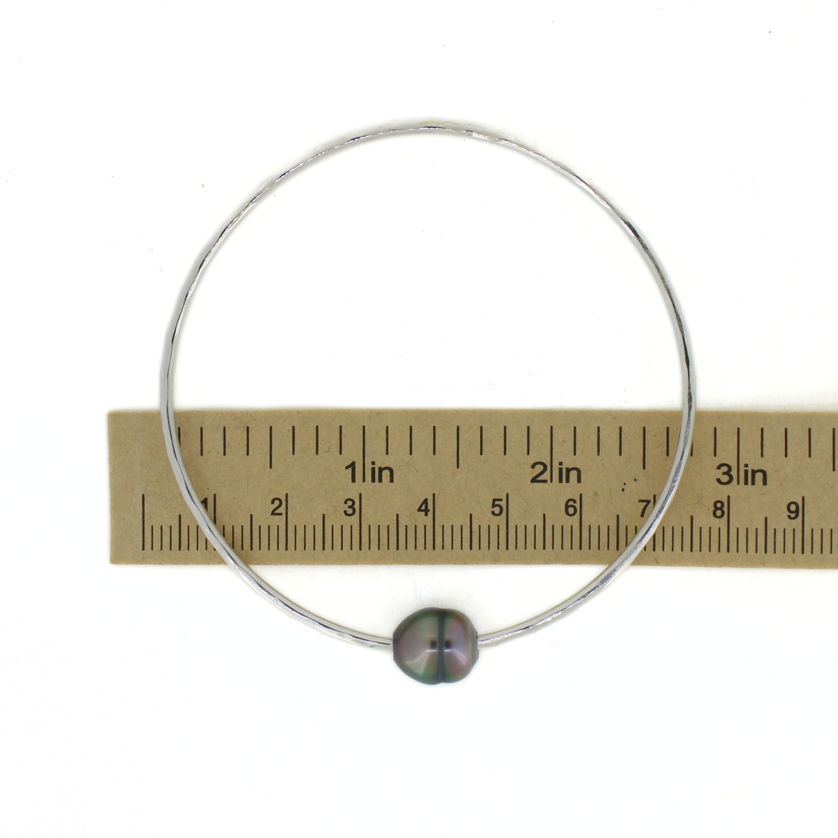 Round silver Tahitian pearl bangle bracelet shown over a ruler for size reference 