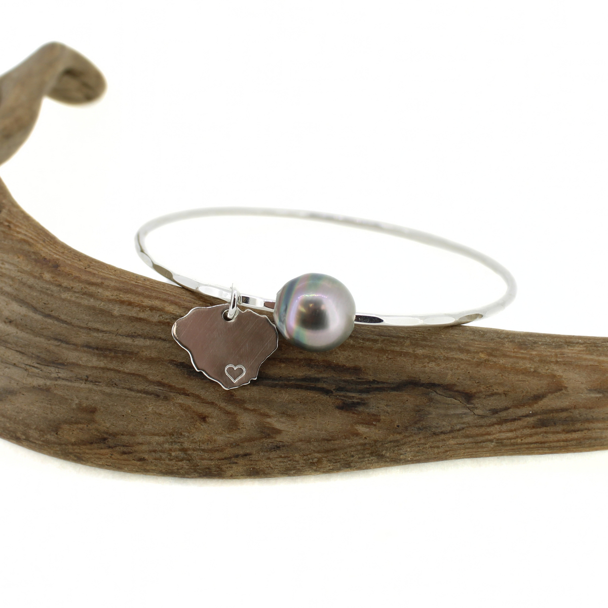 Sterling silver bangle bracelet with a colorful Tahitian pearl and a Kauai island charm displayed on a piece of driftwood 