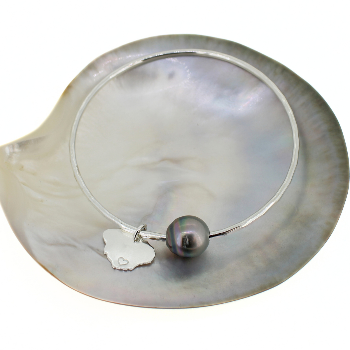 Silver bangle bracelet with a Tahitian pearl and Kauai island charm displayed on a mother of pearl shell