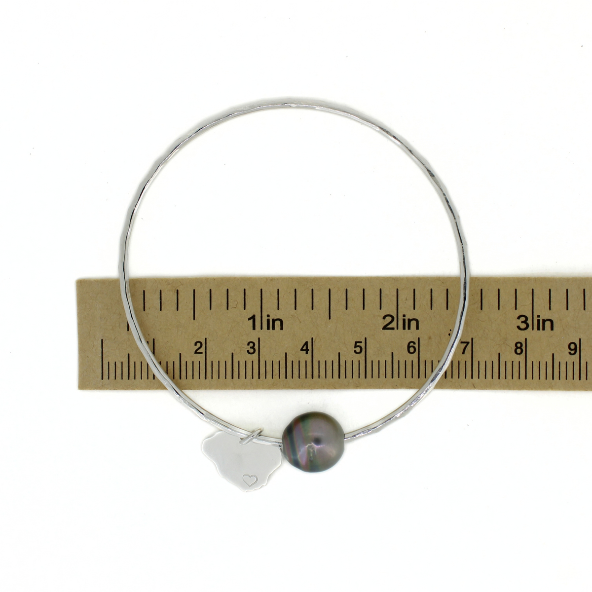 Silver round bangle bracelet with a Tahitian pearl and Kauai island charm shown over a ruler for size reference 