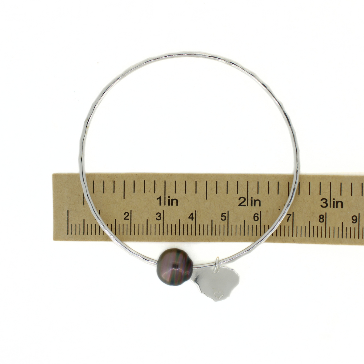 Silver round bangle bracelet with a Tahitian pearl and Kauai island charm, shown over a ruler for size reference 