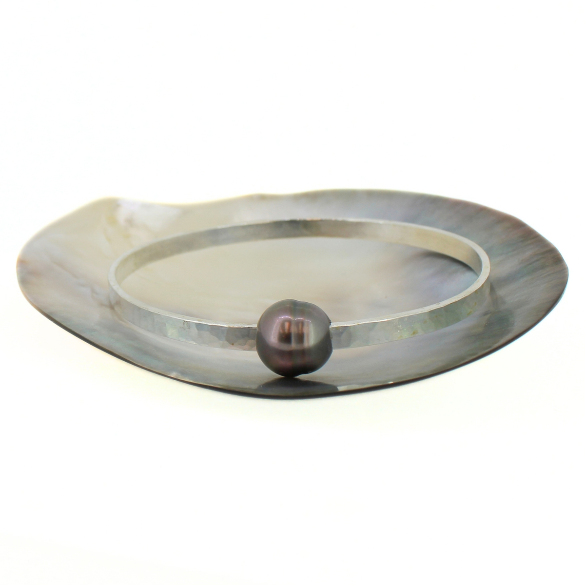 A silver metal bangle bracelet with a single dark, iridescent pearl resting on its outer edge, set against a plain white background.