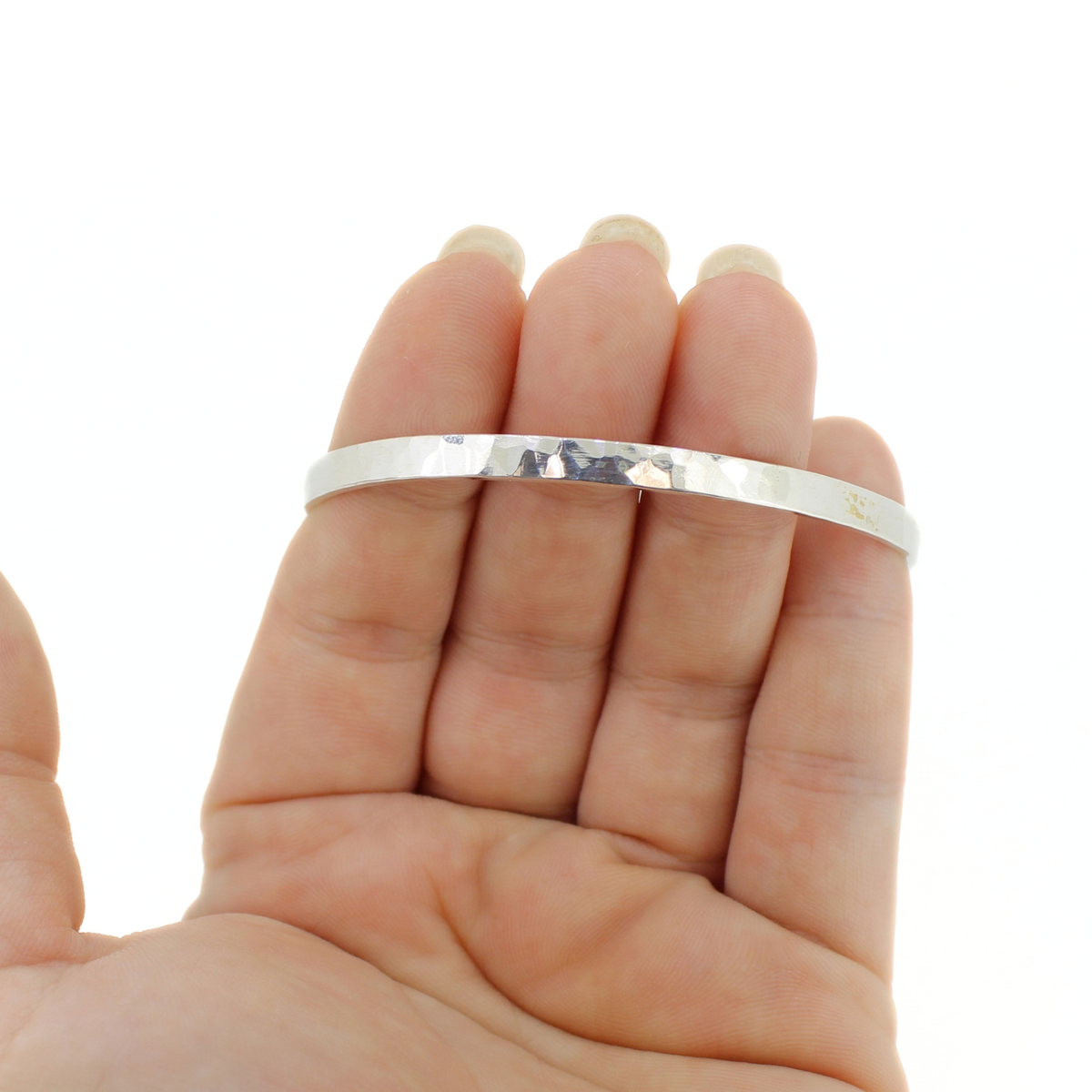 A thick silver bangle bracelet with a hammered texture, held on a person's fingers against a plain white background.