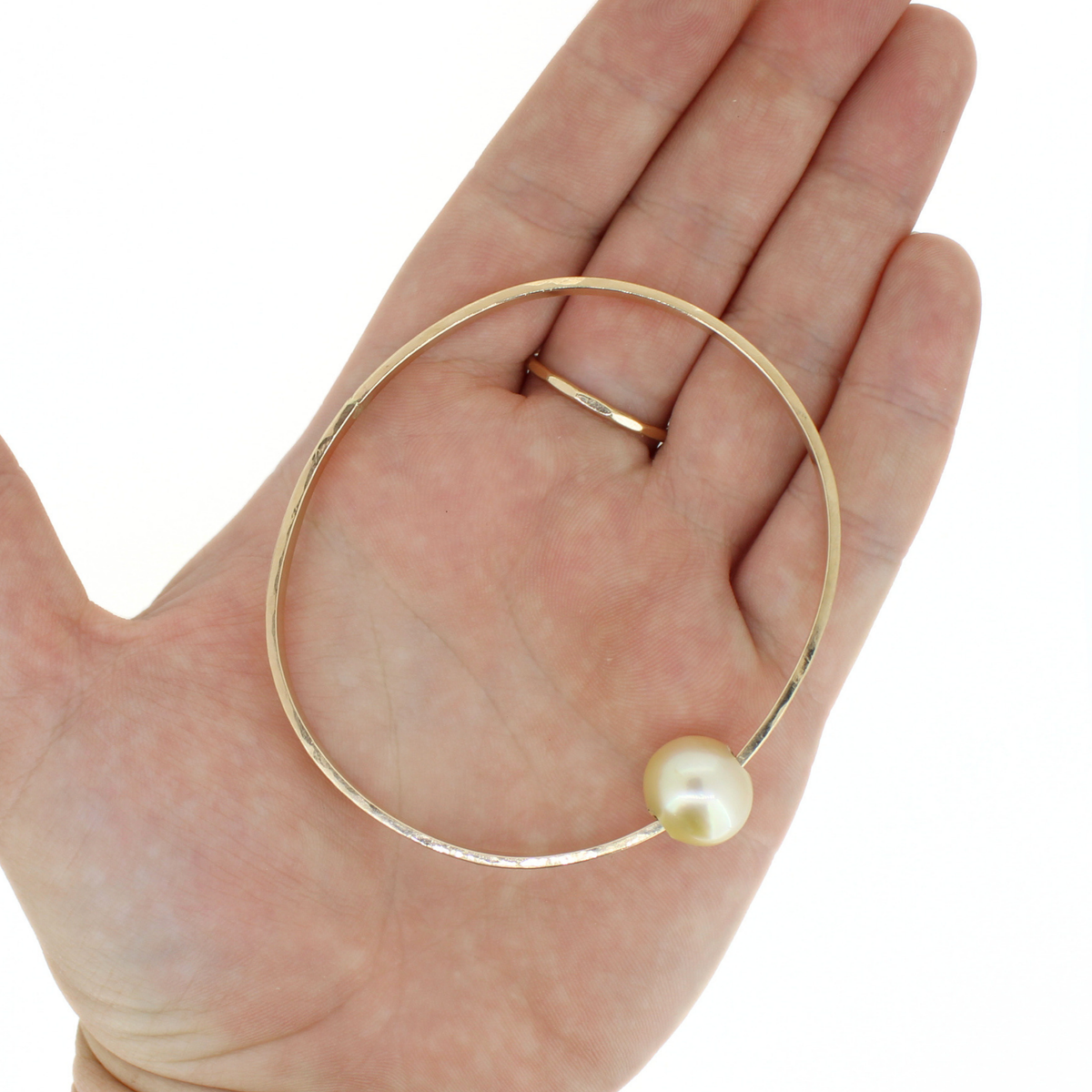 A gold bangle bracelet with a single round pearl, shown resting on an open hand for scale against a white background.