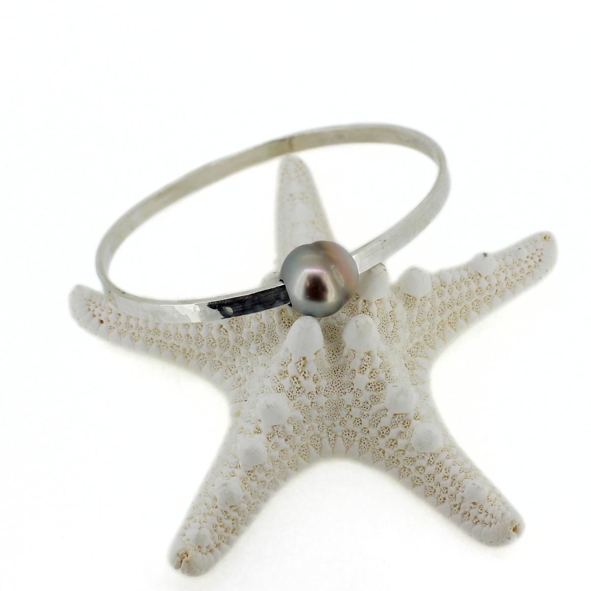 A thick sterling silver Tahitian pearl bangle displayed on a starfish against a white background