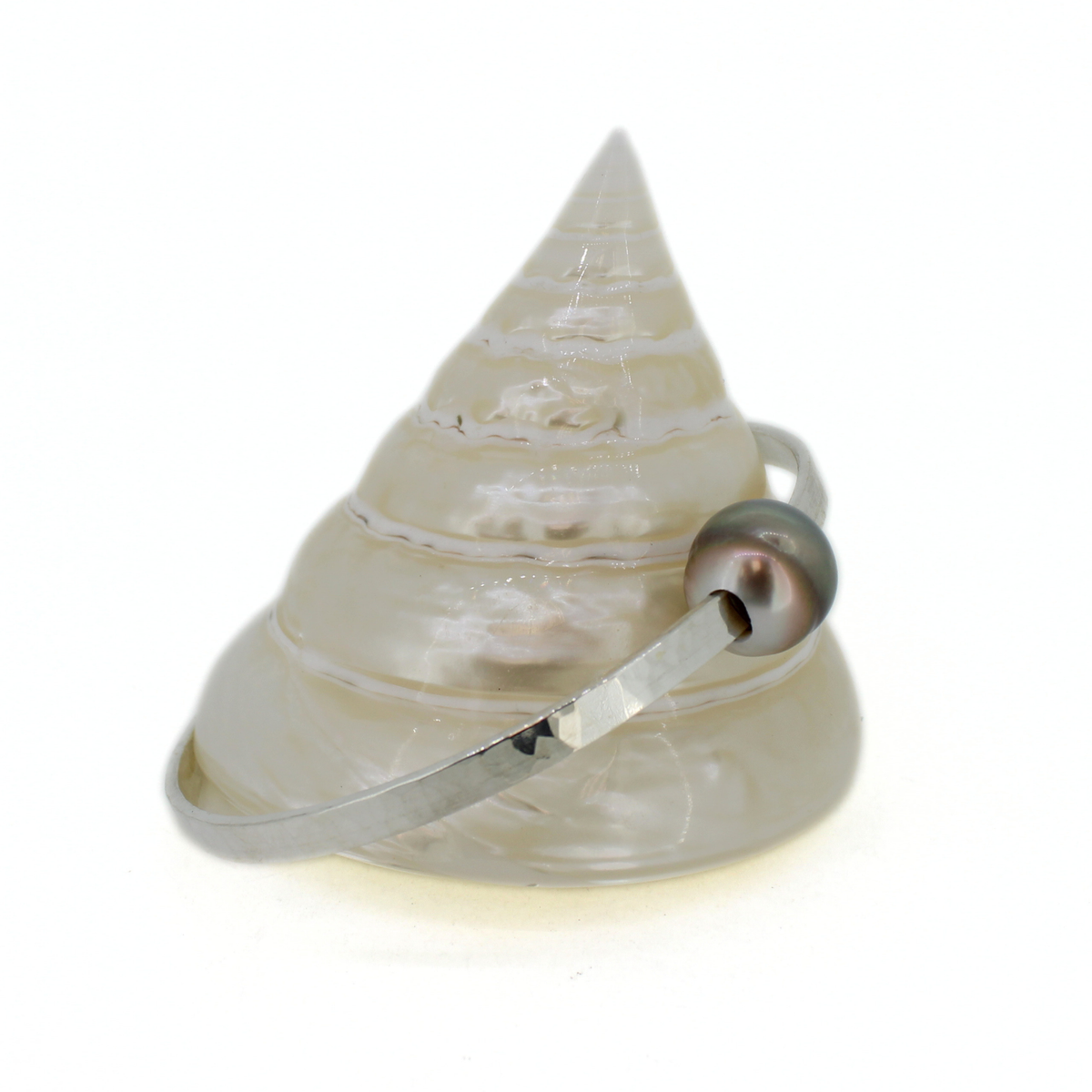 A silver pearl bangle displayed on a white seashell against a white background