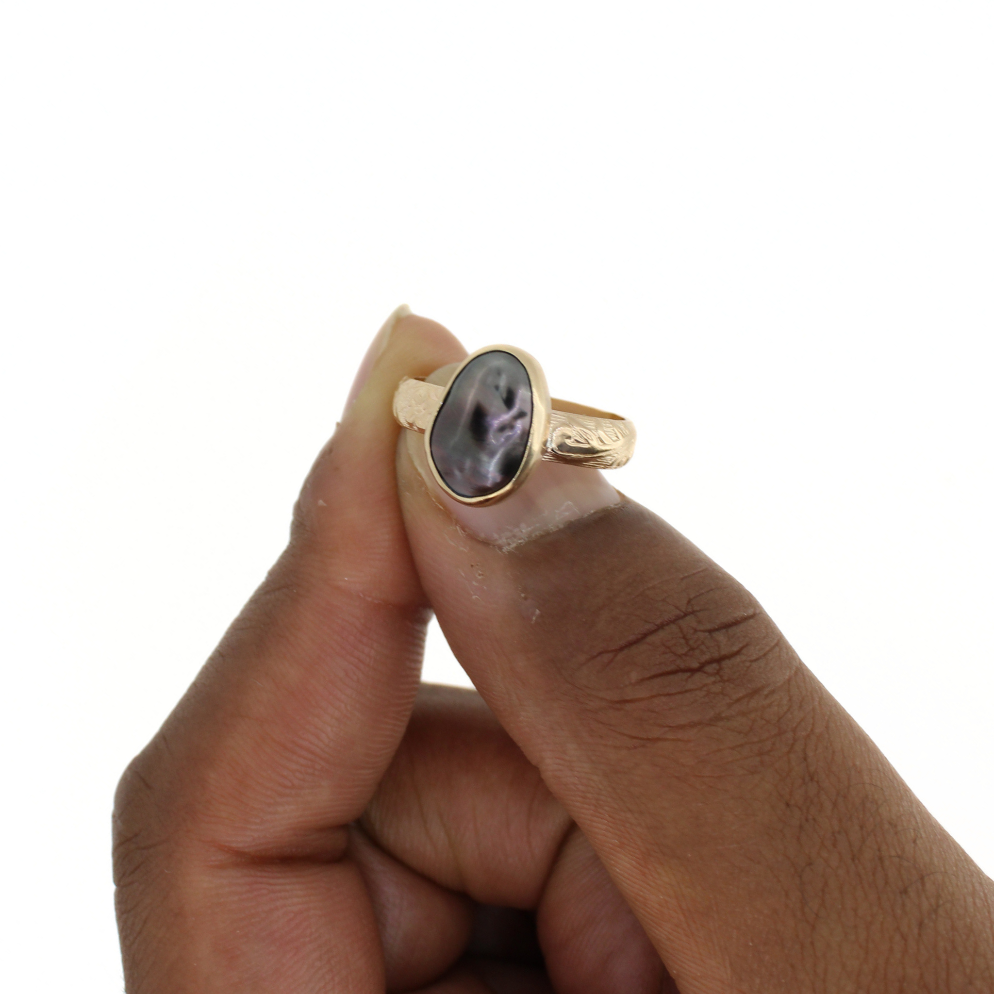 Gold ring held between fingers, oval dark keshi pearl bezel