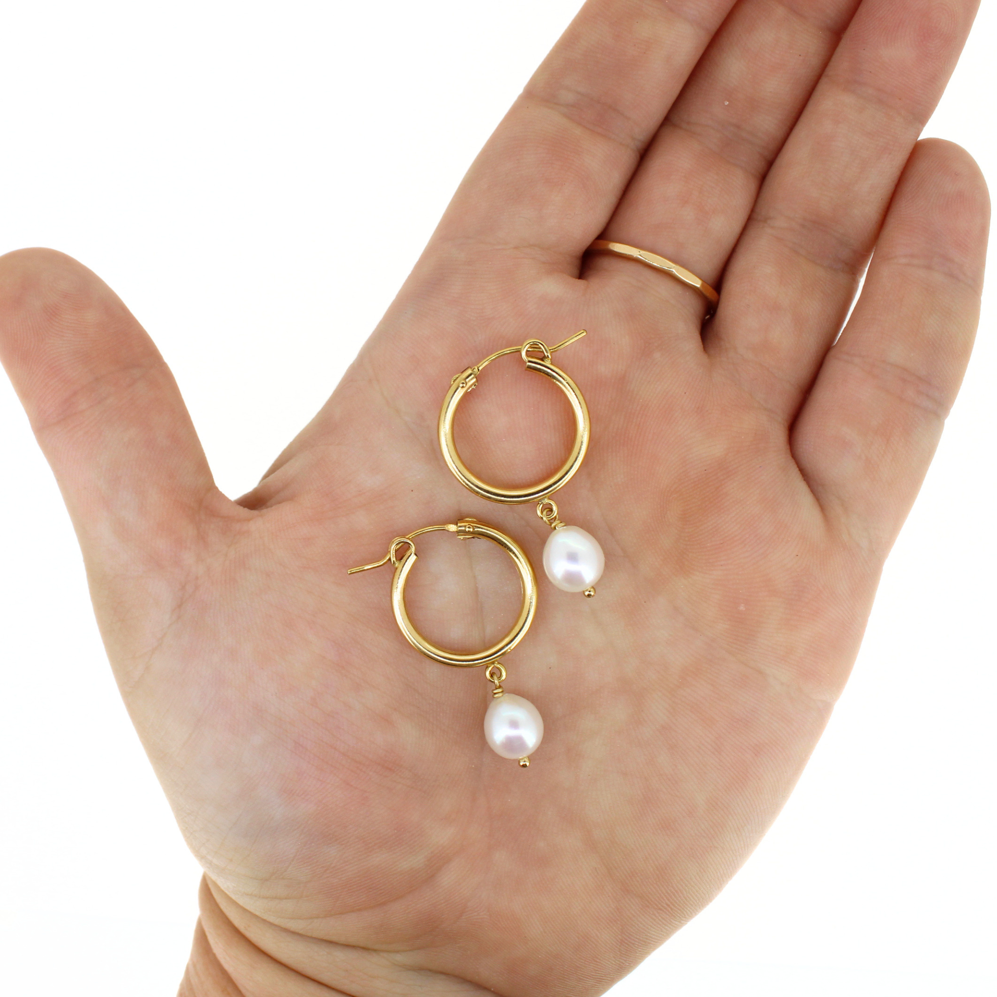 A pair of gold hoop earrings with dangling white freshwater pearls, displayed on an open hand against a white background.