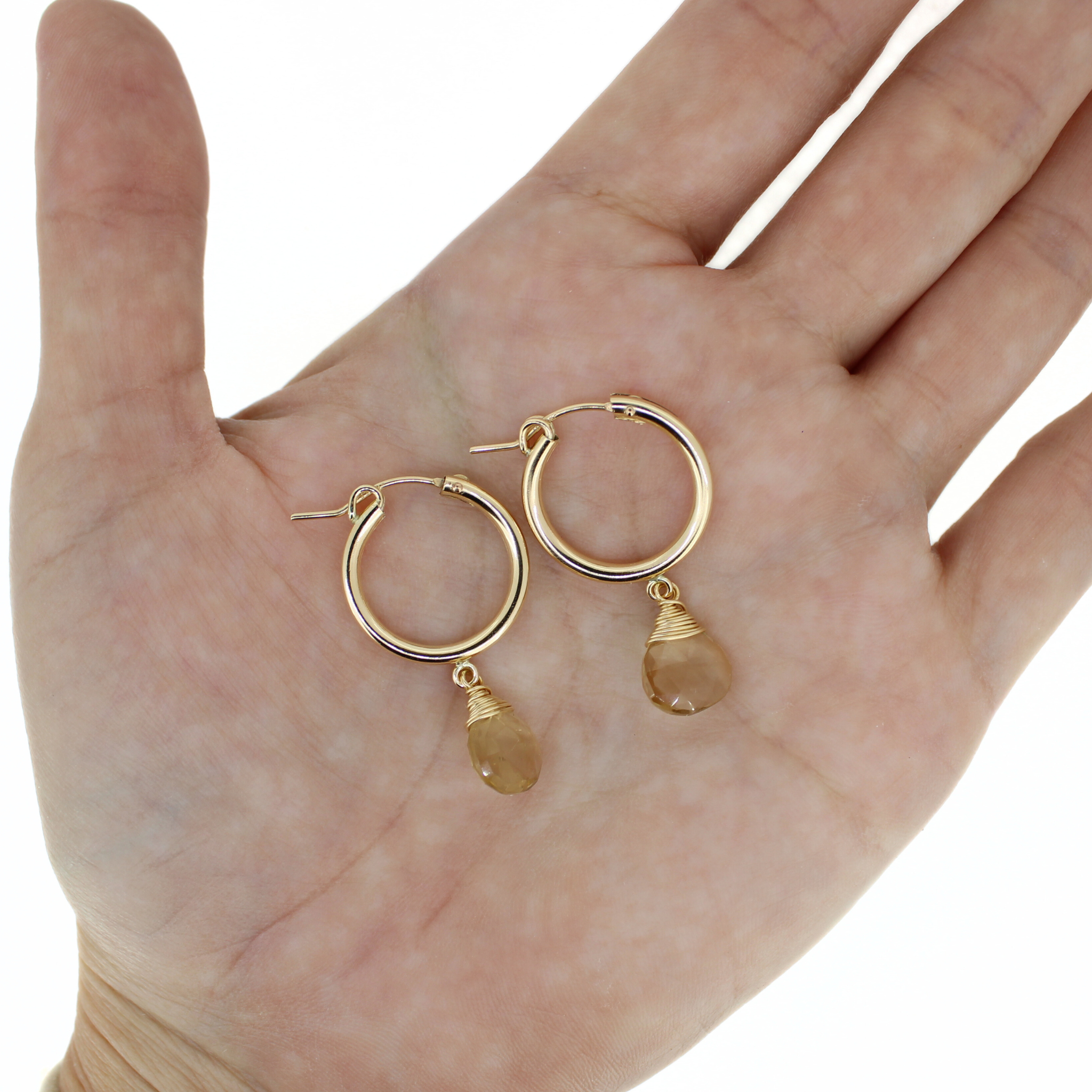 Gold hoop earrings with champagne topaz dangle charms, on open palm