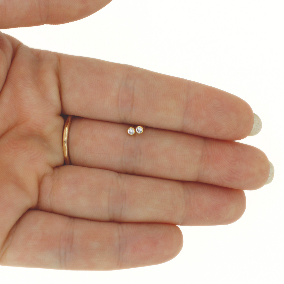 A persons hand holding a pair of tiny gold round CZ stud earrings