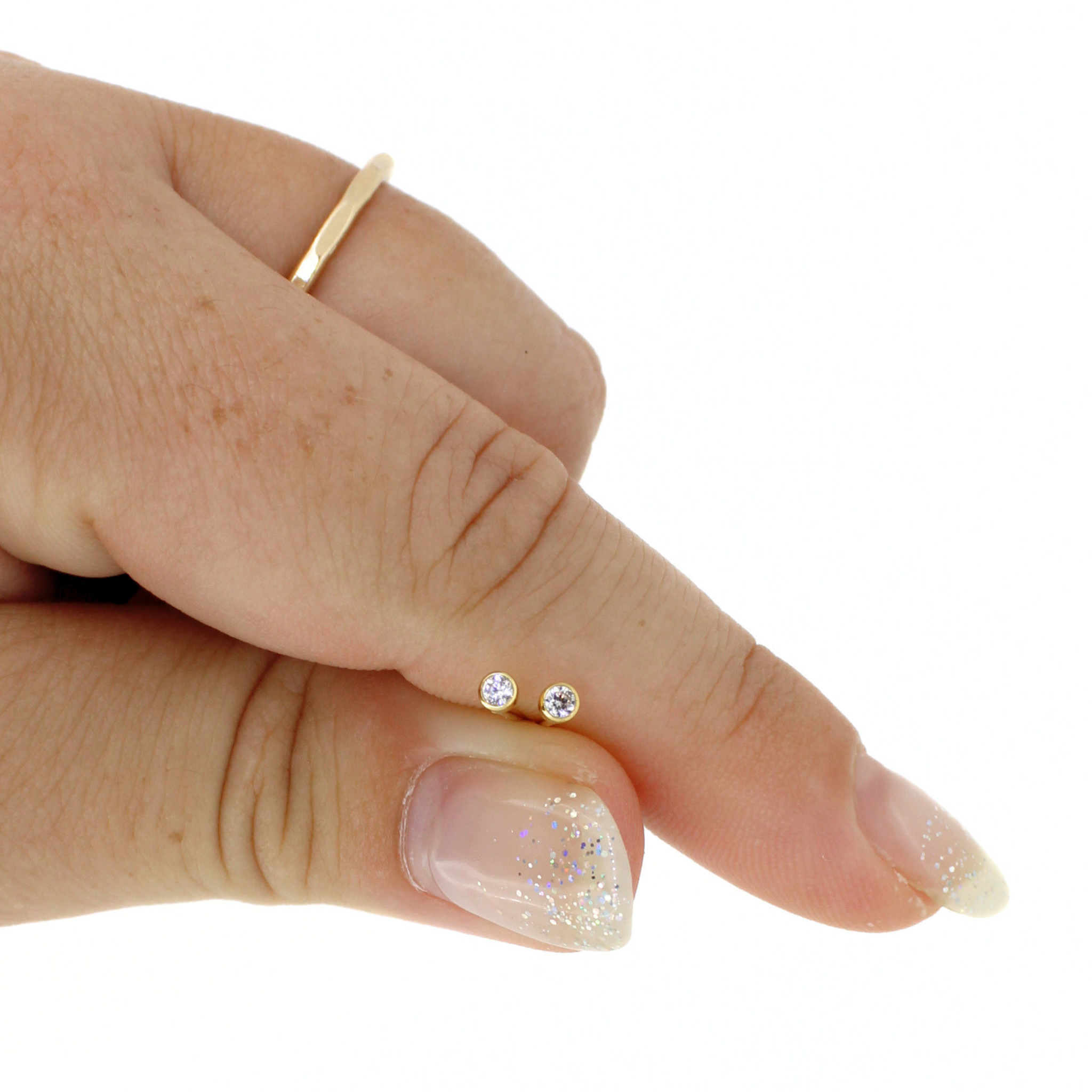 A close-up of a hand holding a pair of small round stud earrings against a plain white background.
