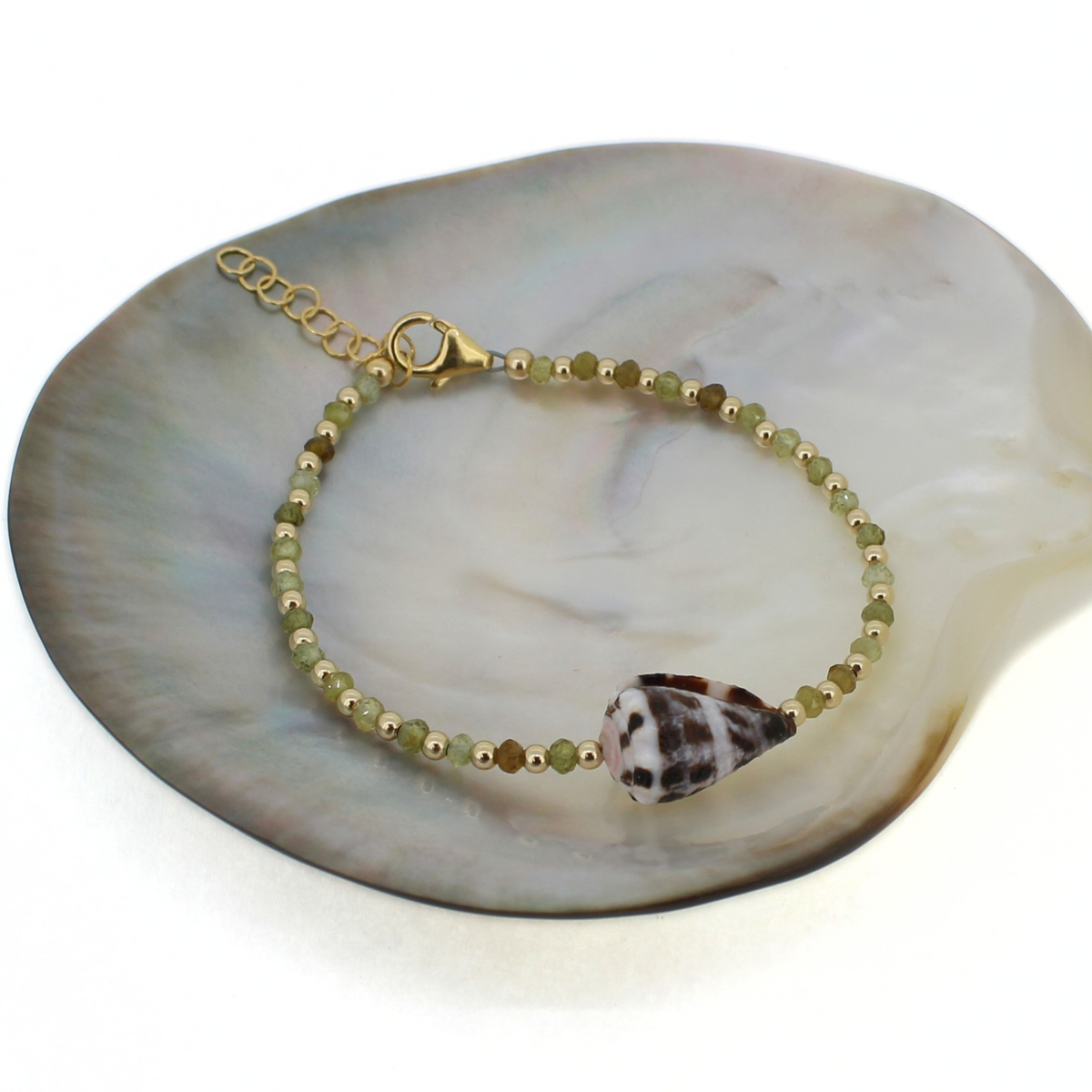 Gold beaded green garnet bracelet featuring a spotted Hebrew cone shell at the center. Displayed on a mother of pearl shell 