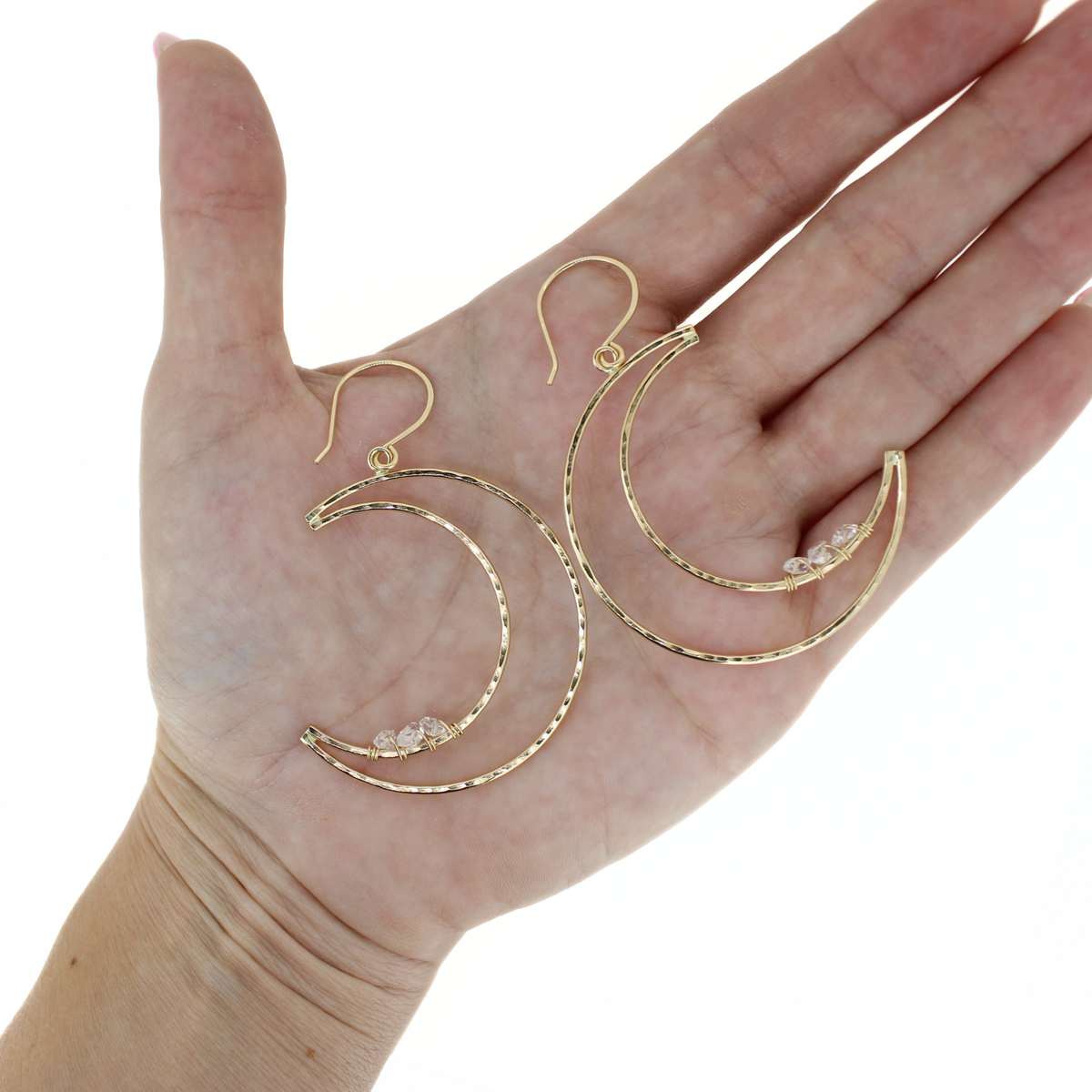A pair of gold crescent-shaped hoop earrings with small clear crystal accents, displayed on an open hand against a white background.