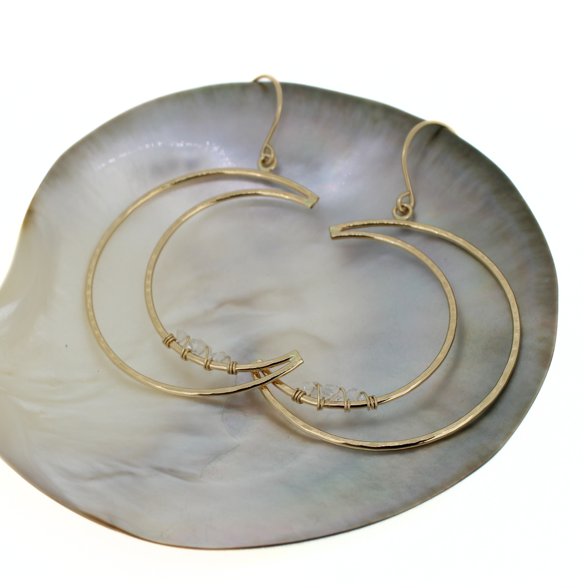 Gold crescent moon hoop earrings with small clear crystal accents, displayed on a white shell dish against a white background.