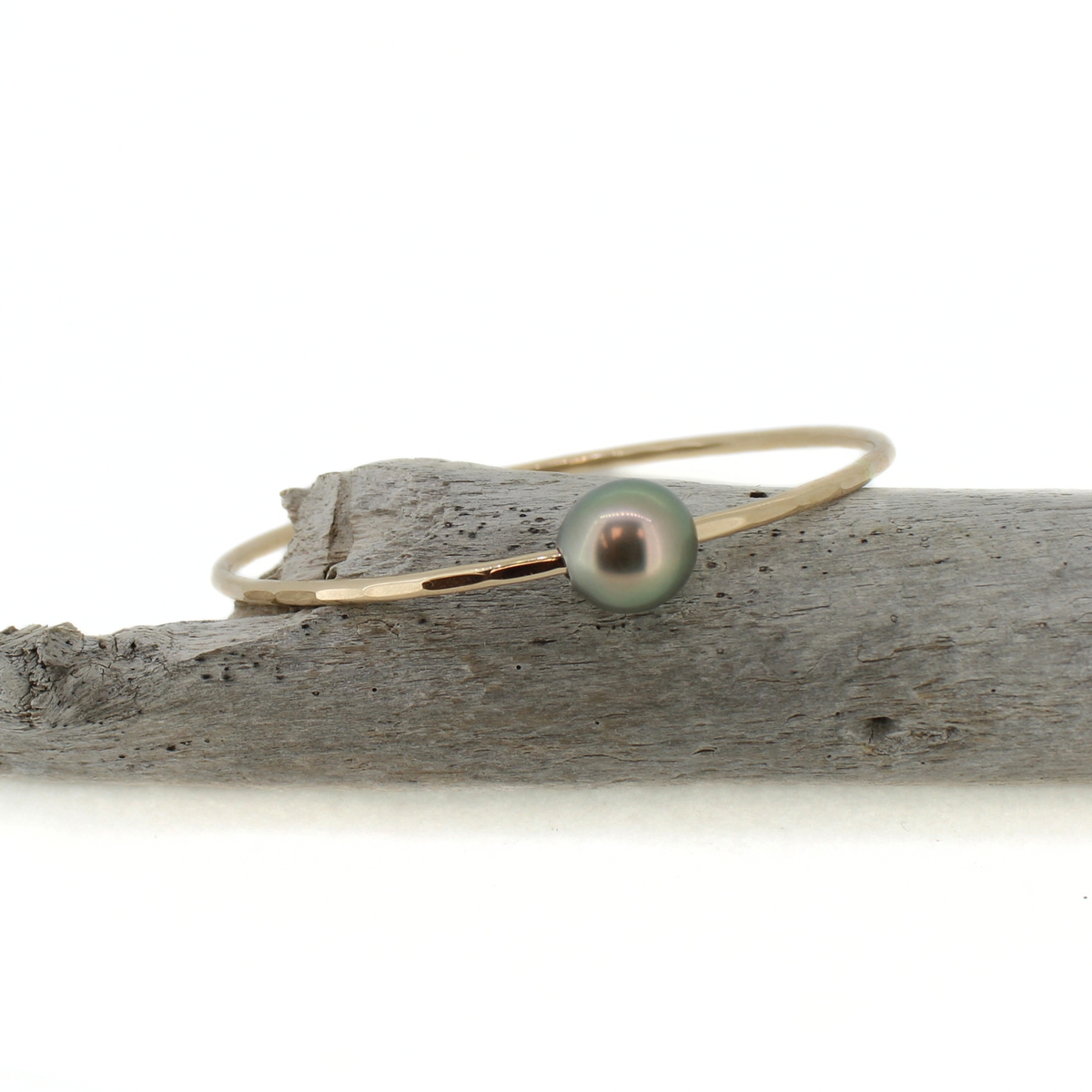 Gold Tahitian pearl bangle bracelet displayed on a piece of driftwood 