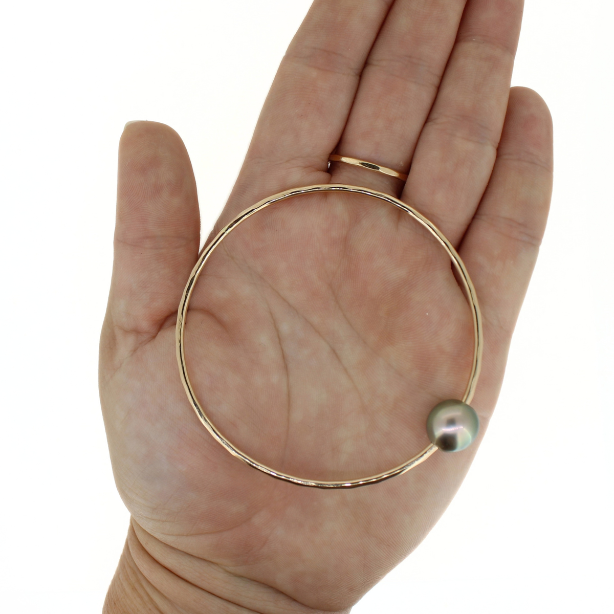 Gold bangle bracelet with a Tahitian pearl displayed on an open palm