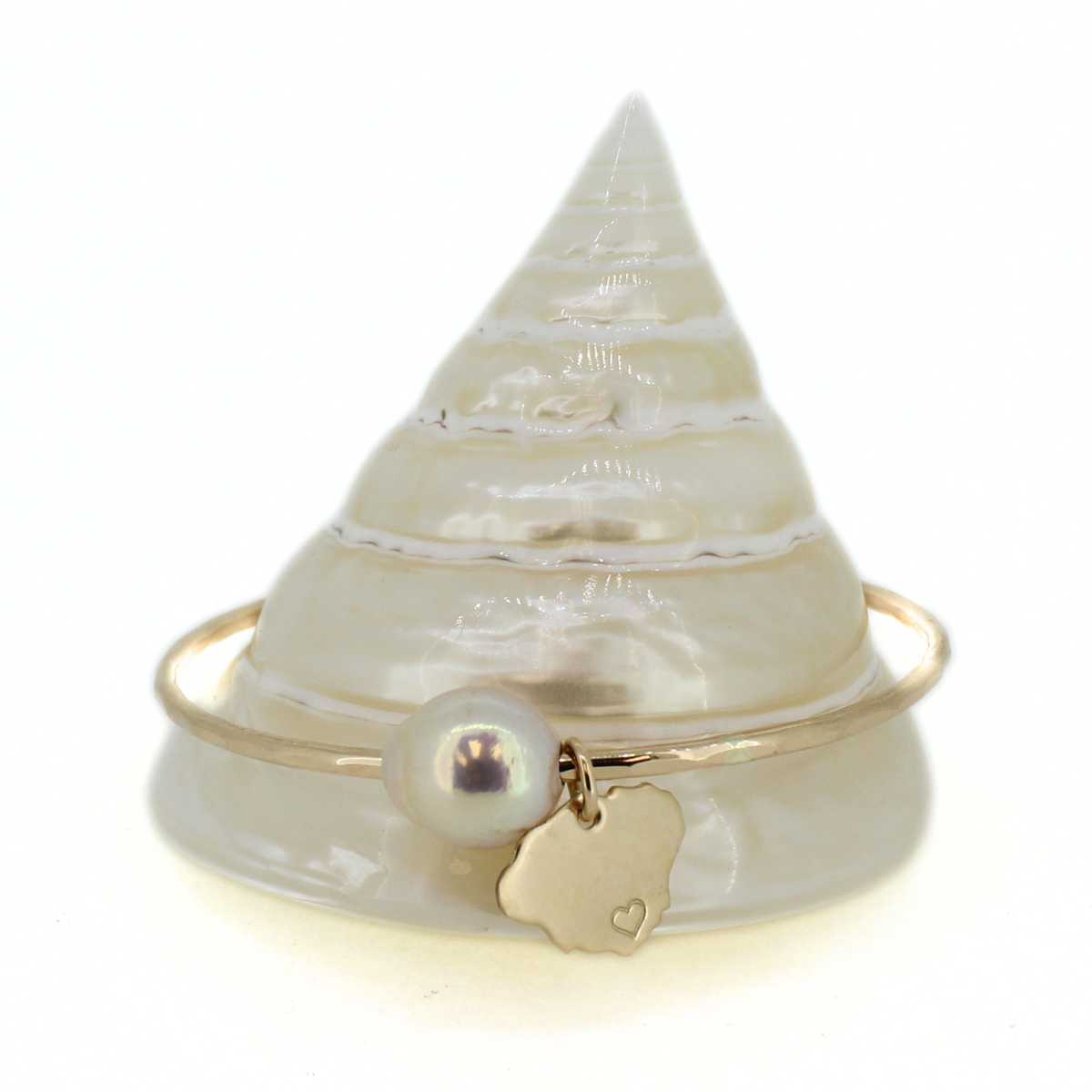 Gold bangle bracelet featuring a white fresh water pearl and Kauai island charm displayed on a cone shell