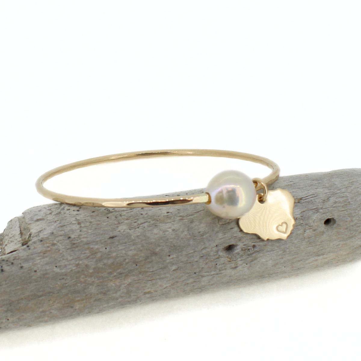 Gold bangle with a hammered texture and a white Edison pearl and Kauai island charm on a piece of drift wood