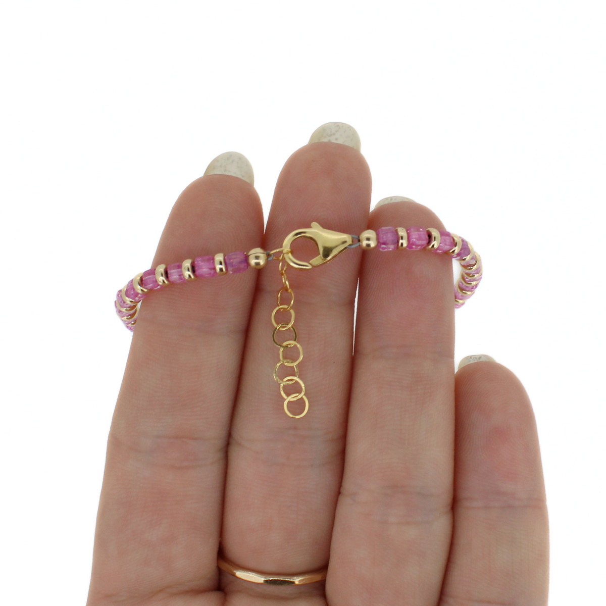 A gold beaded bracelet with pink faceted  gemstone beads and a lobster clasp, held on a person's fingers against a plain white background.
