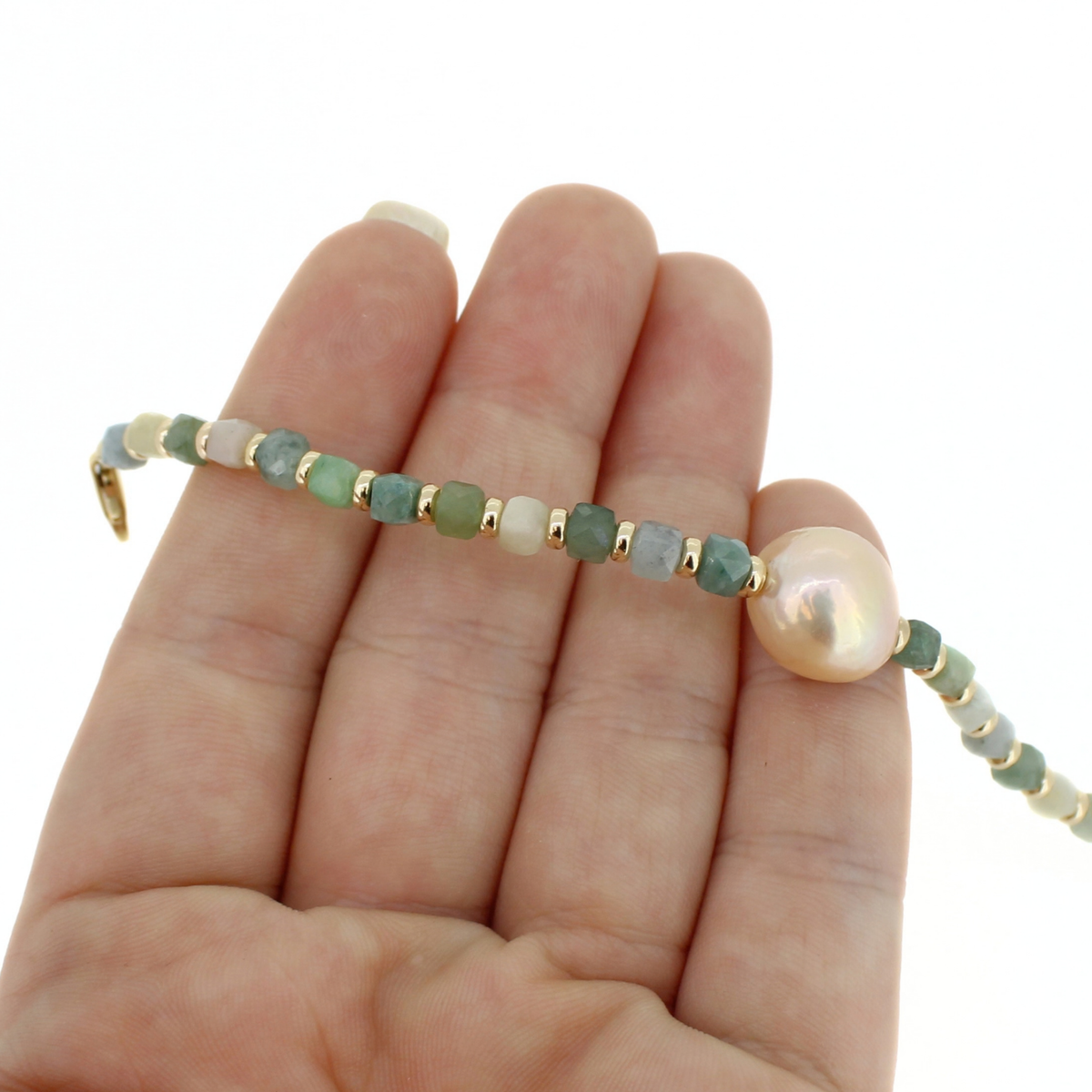 Gold beaded jade bracelet with a large fresh water pearl shown on a persons hand.