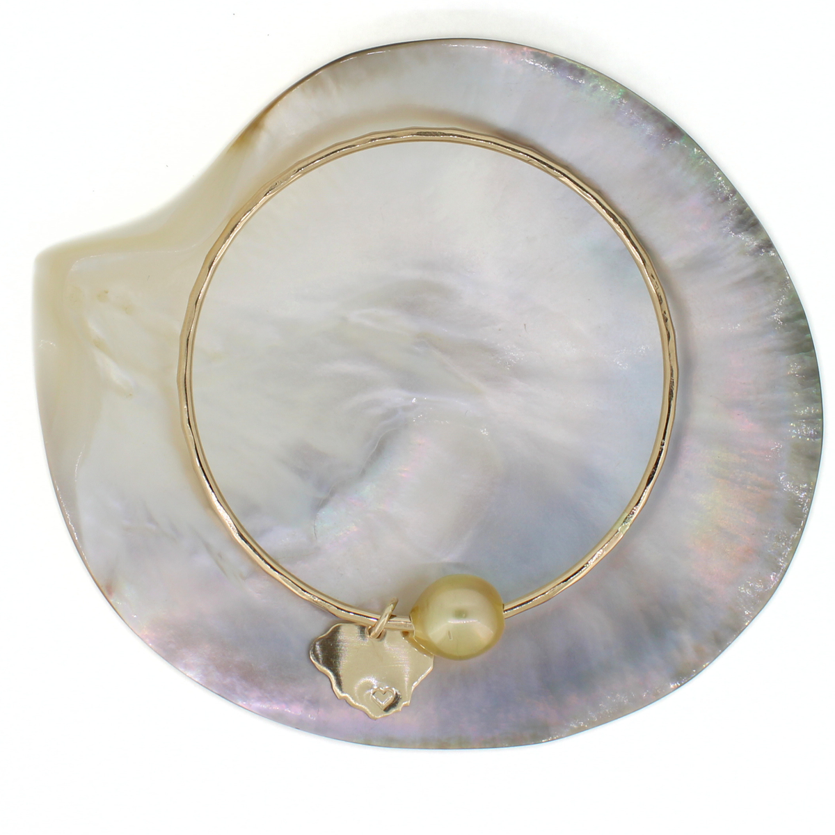 Gold pearl bangle displayed on a iridescent shell against a white background