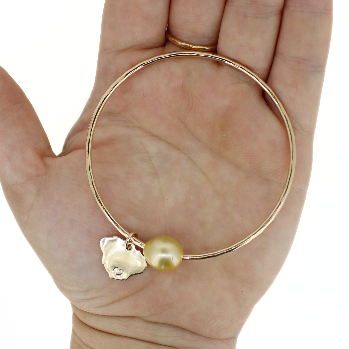 Gold south sea pearl bangle bracelet with Kauai island charm displayed on an open hand