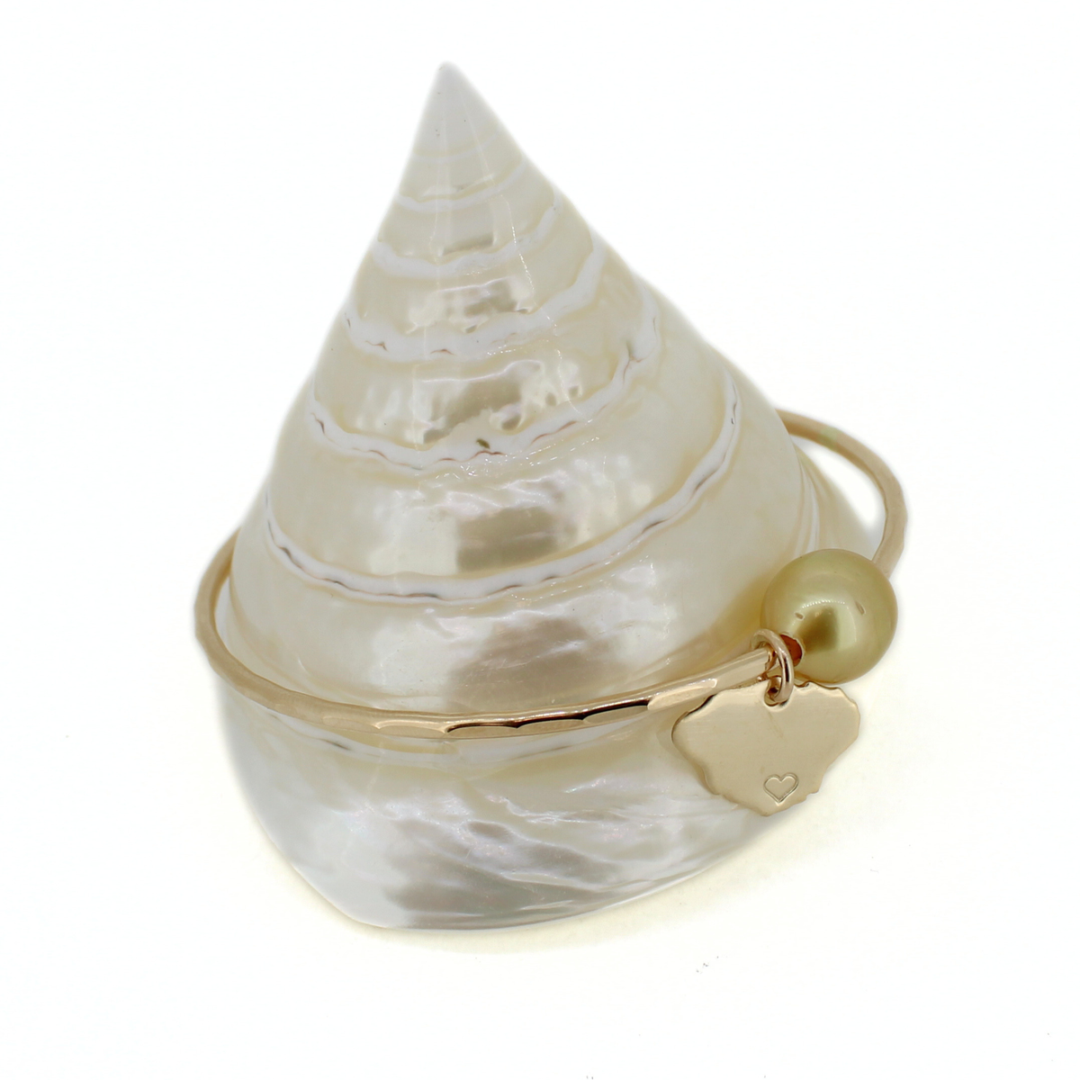 Gold bangle bracelet with a golden south sea pearl and Kauai island charm displayed on a cone shell with a white background