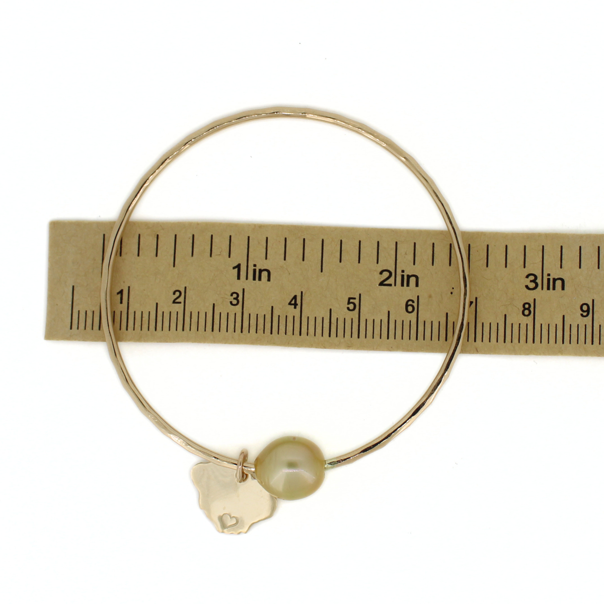 Gold round bangle bracelet over a ruler for size reference