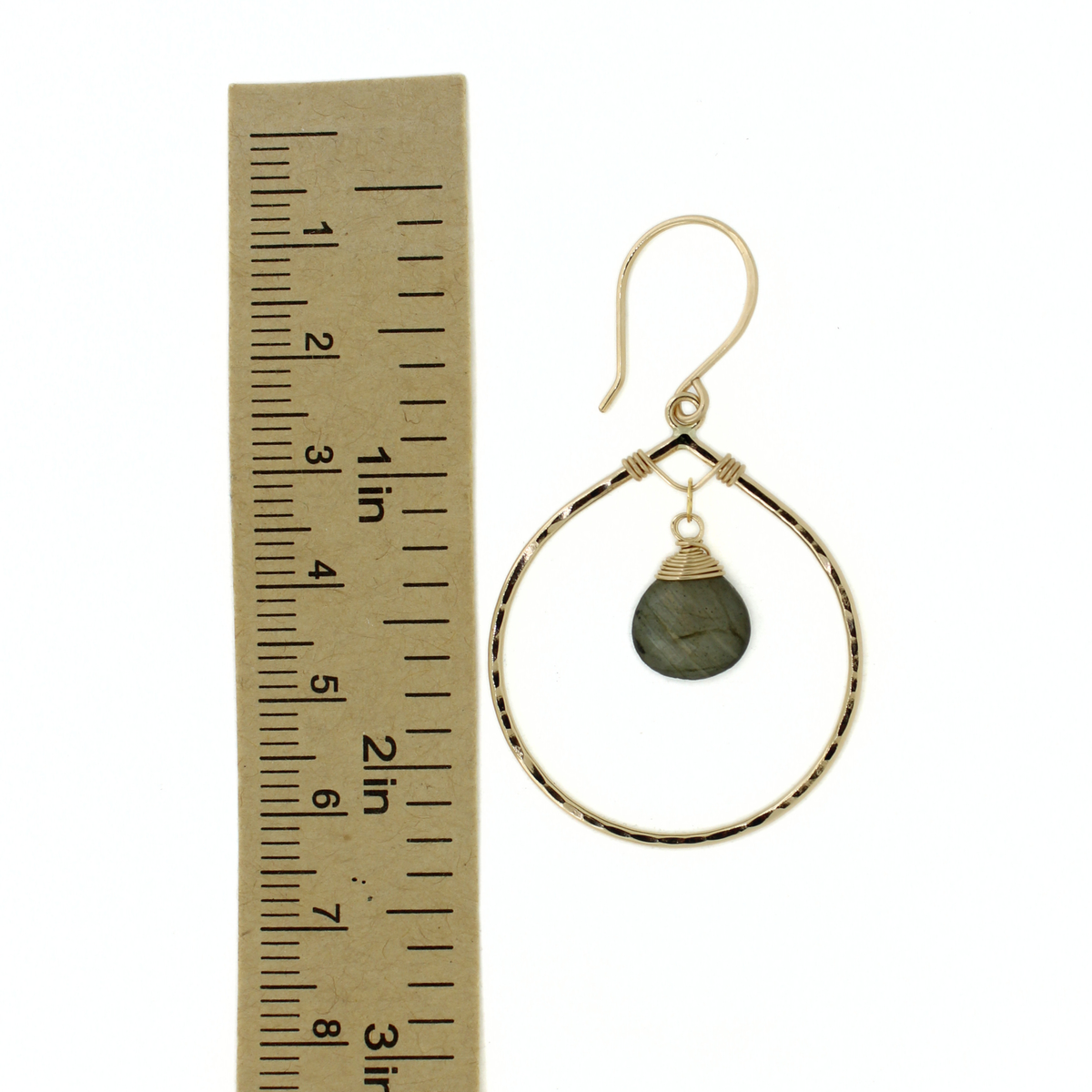 Gold hoop dangle earrings with a small dark gray stone, shown next to a cardboard ruler for scale on a white background.