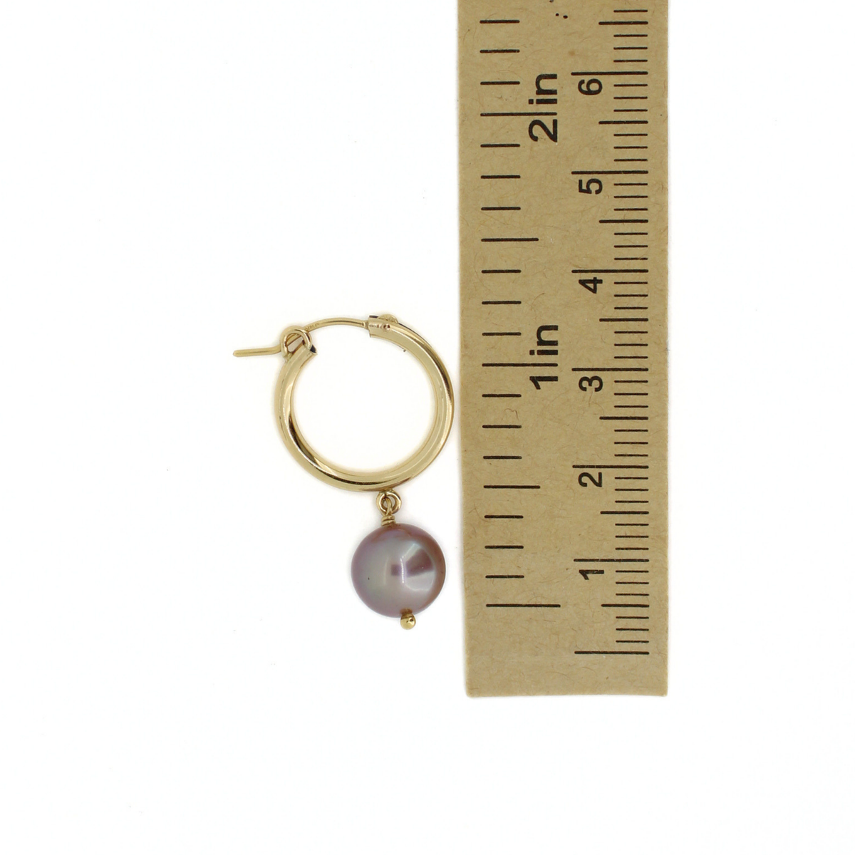 A single gold hoop earring with a dangling round pearl, shown next to a paper ruler for scale on a white background.