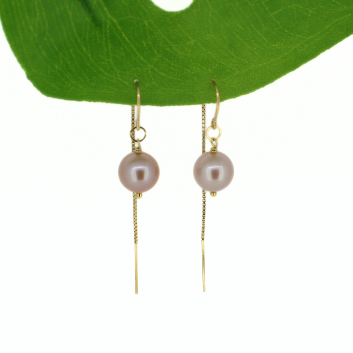A pair of gold drop earrings with round pale pink freshwater pearls and long dangling chains, displayed against a white background with a green leaf at the top.
