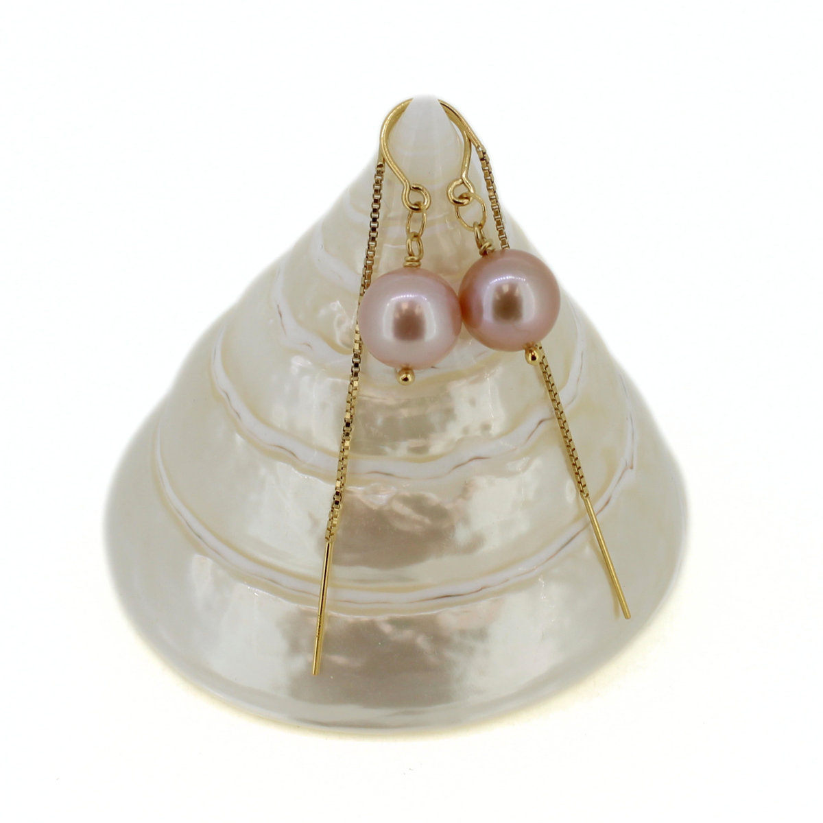 A pair of gold drop earrings with round pink freshwater pearls, displayed on a white seashell stand against a white background.