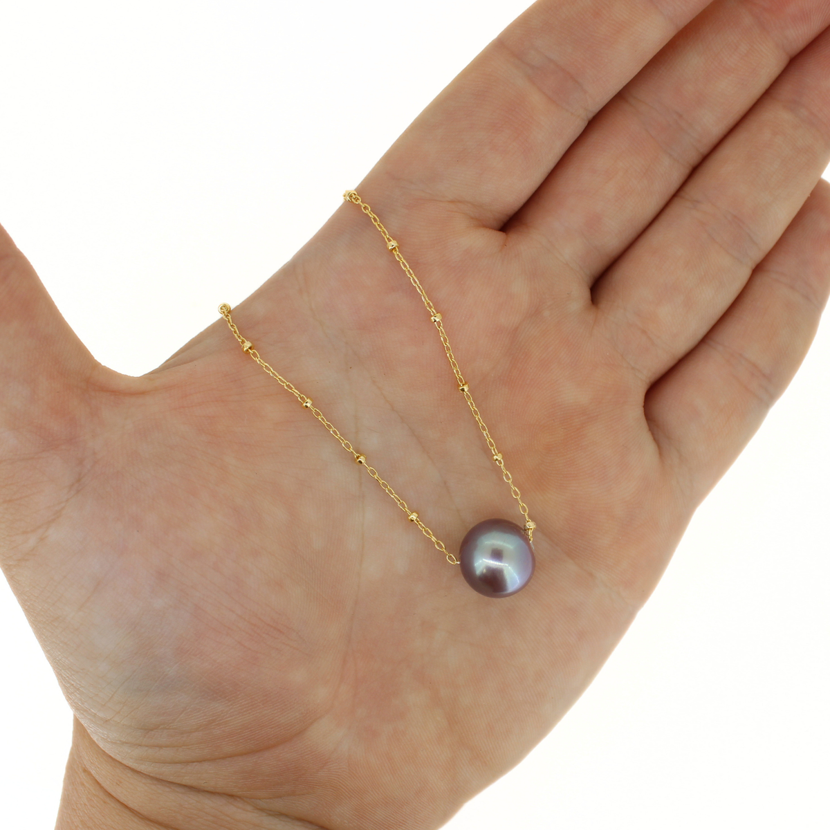 A gold chain necklace with a single round iridescent pearl pendant, displayed on an open hand against a white background.
