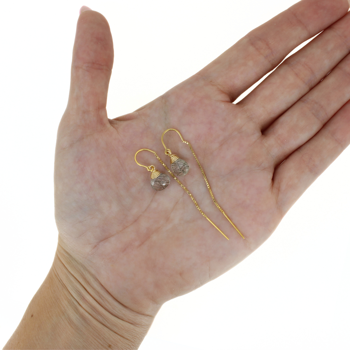 A pair of gold drop earrings with rutile quartz gemstone pendants, displayed on an open hand against a white background.