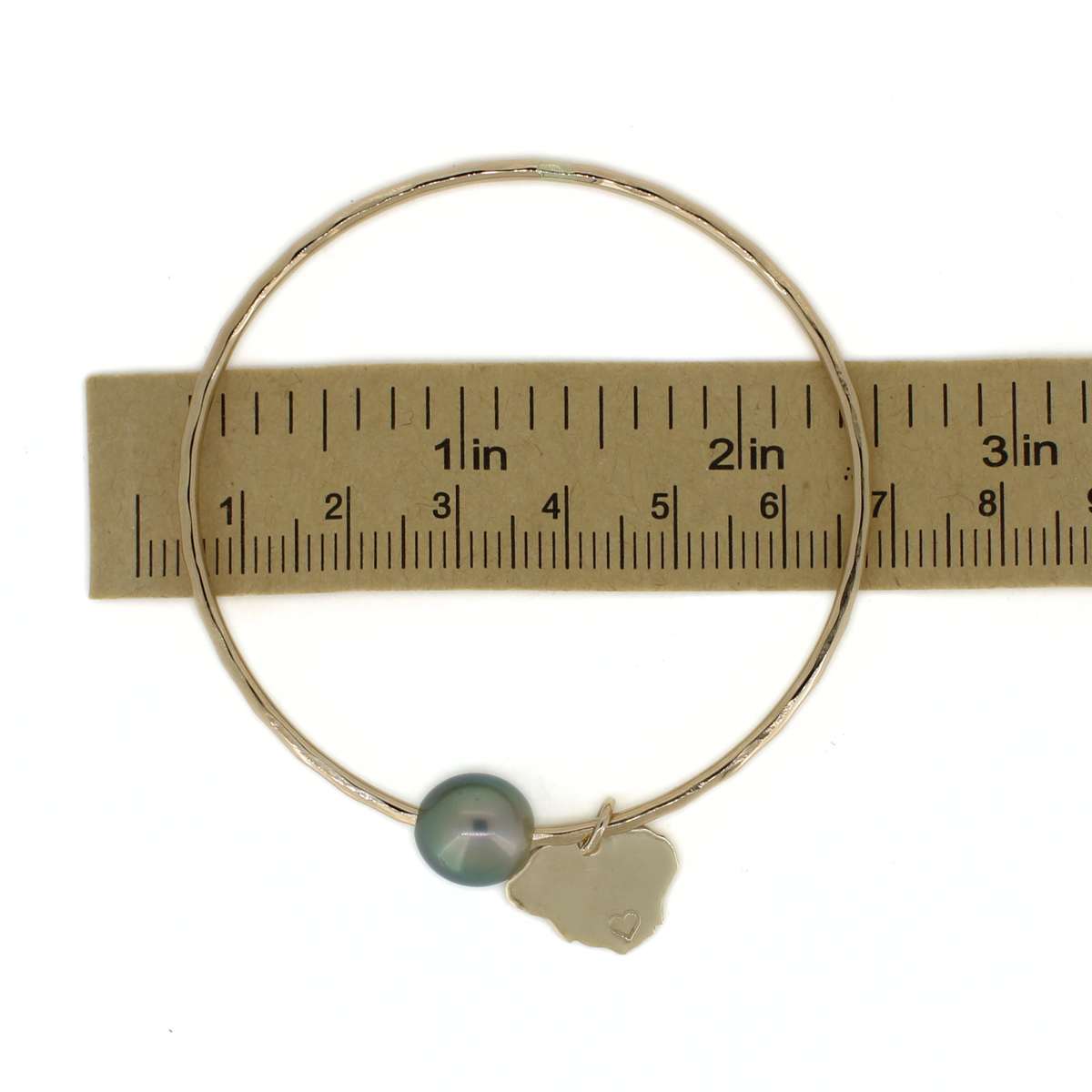 Gold bangle bracelet over a ruler for size reference 