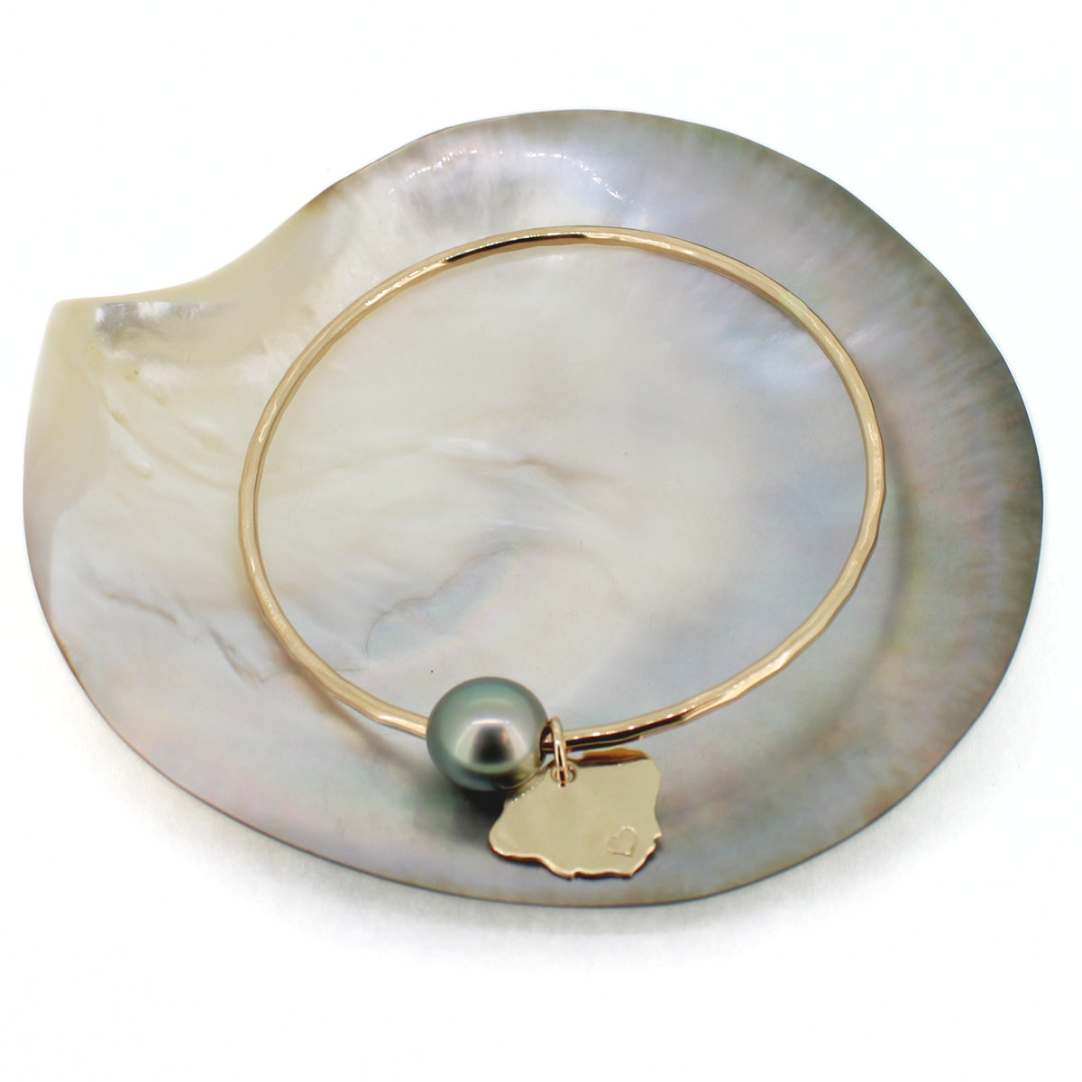 Gold Tahitian pearl and Kauai charm round bangle bracelet displayed on a shell abasing a white background