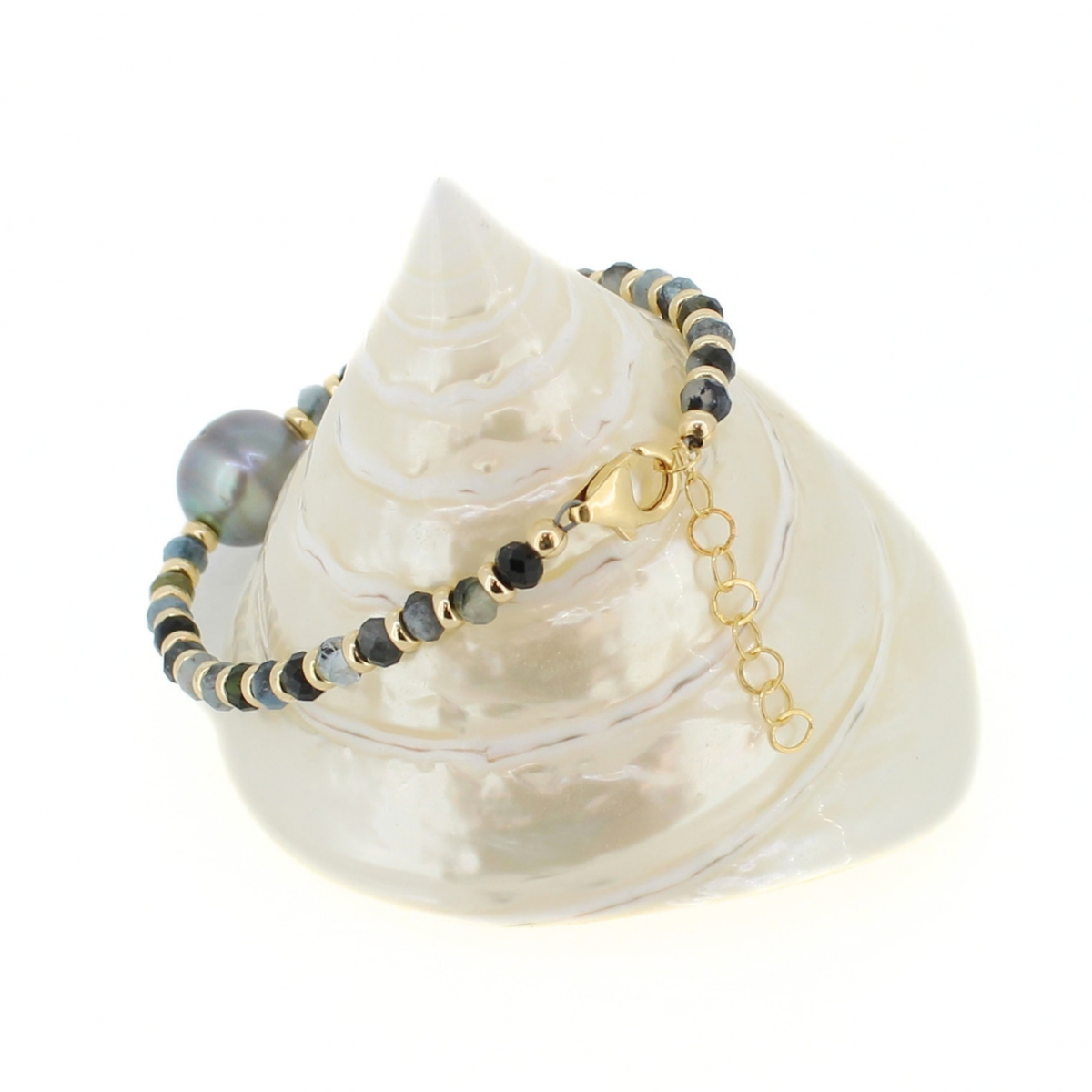A beaded bracelet with a large iridescent pearl and small gold spacer beads, displayed on a white seashell against a white background.