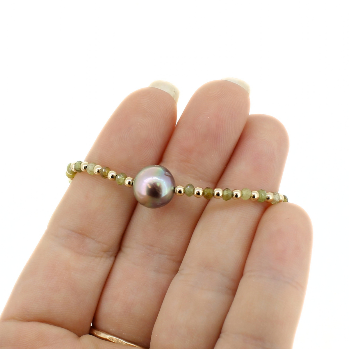 A close-up of a hand holding a delicate beaded bracelet with a large iridescent pearl at the center, set against a plain white background.