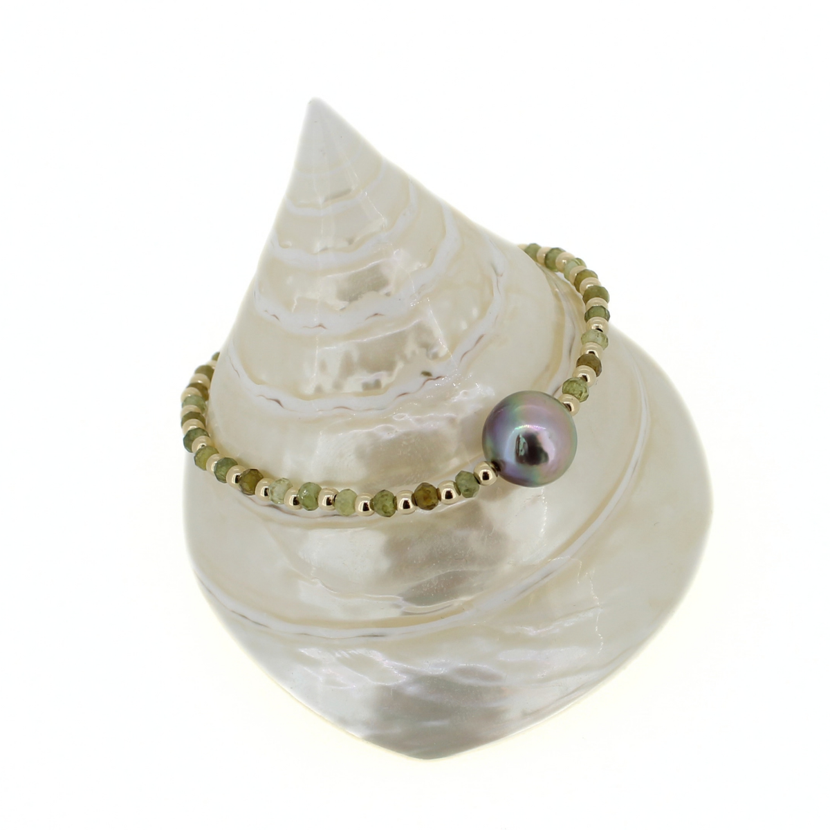 A beaded bracelet with olive green faceted beads and a single iridescent pearl, displayed on a white seashell stand against a white background.
