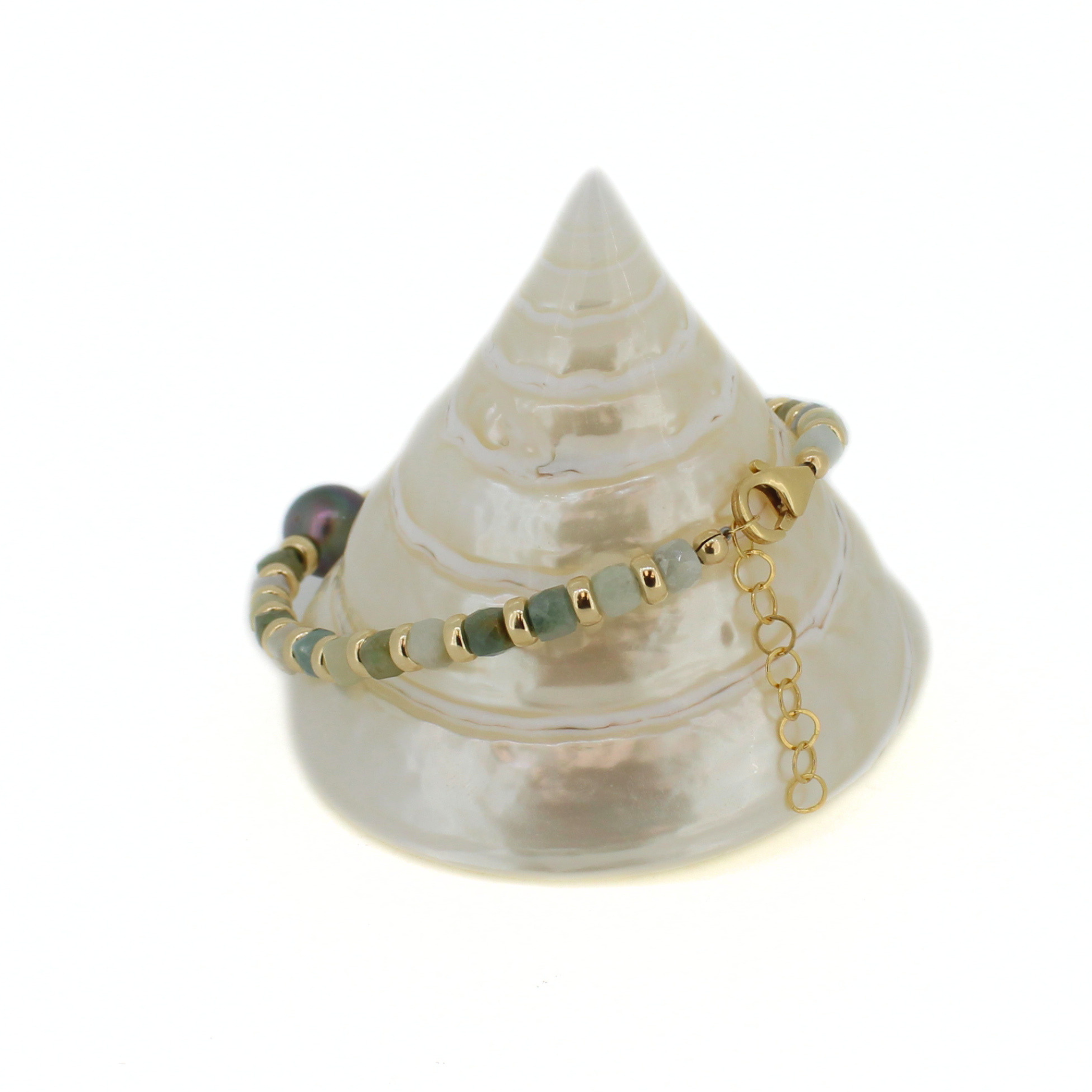 A beaded bracelet with gold-toned metal beads, light green stone beads, and a dark iridescent bead, displayed on a white seashell stand against a white background.