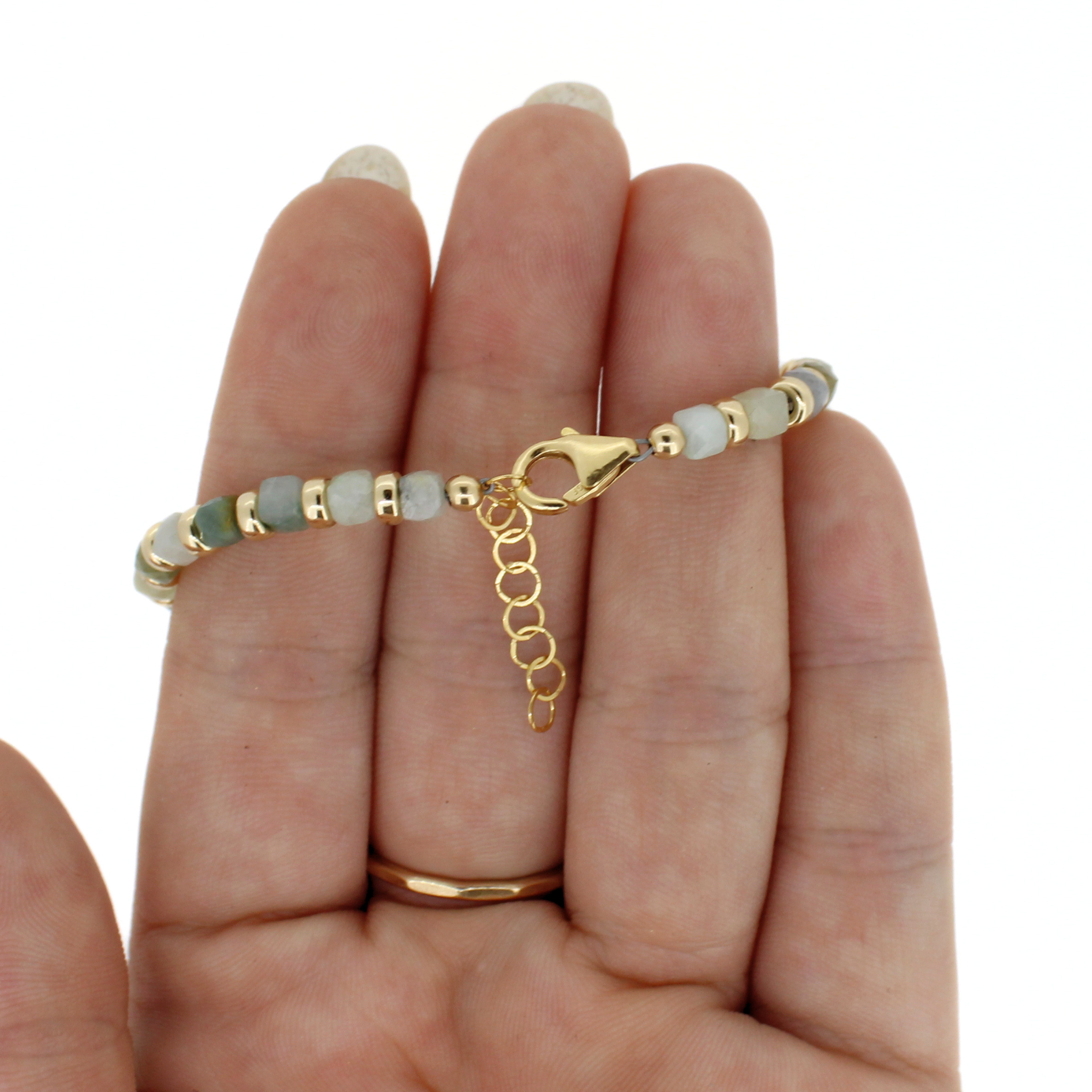 A delicate beaded bracelet with light green and white beads, gold spacer beads, and a gold lobster clasp, shown worn on a person's hand against a white background.