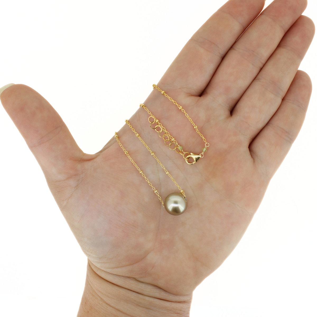 A gold dainty necklace with a Tahitian pearl displayed on a persons hand for size reference. 